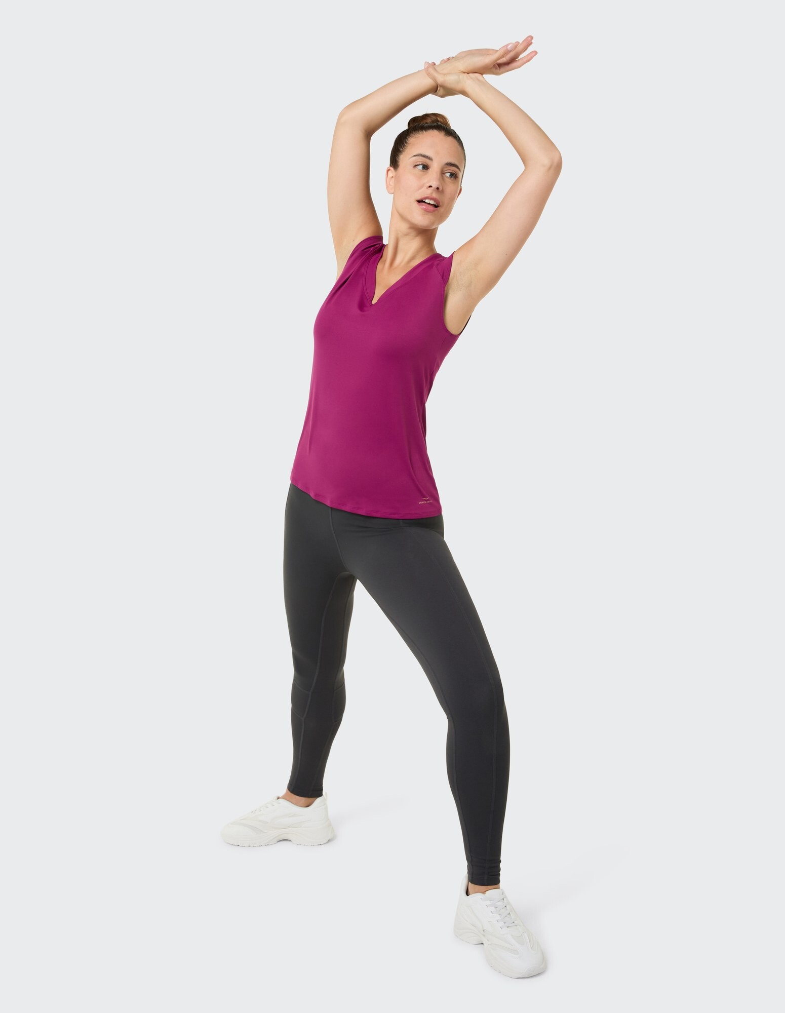 Frau in einem lila ärmellosen Top und schwarzen Leggings streckt sich in einer lässigen Pose.