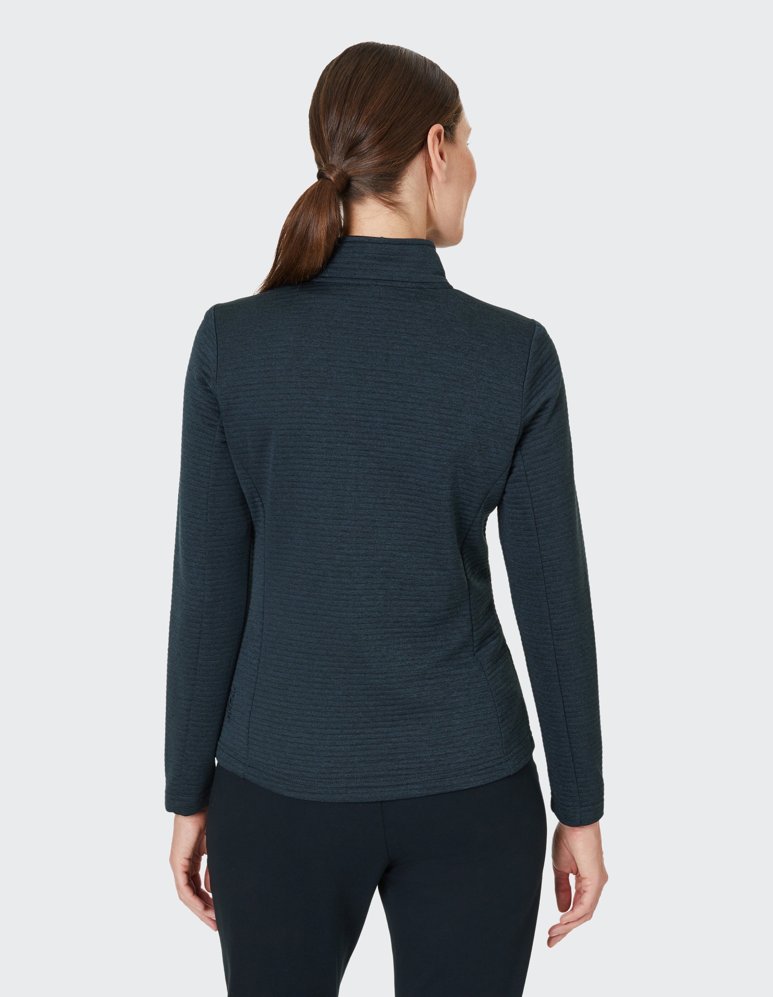 Eine Frau von hinten, trägt einen dunkelblauen, langärmeligen Rollkragenpullover, ihre Haare sind zu einem Pferdeschwanz gebunden.