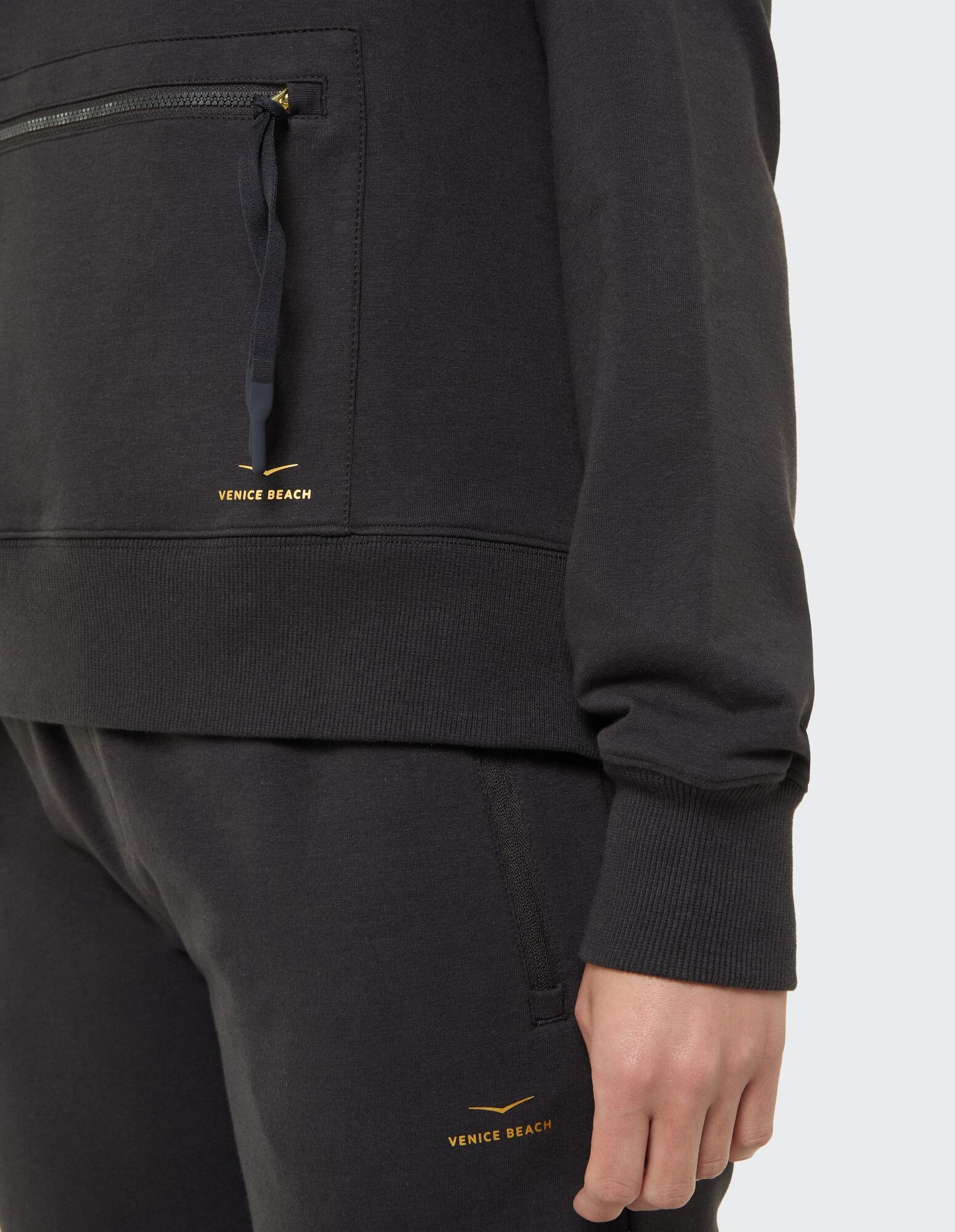 Nahaufnahme eines kuscheligen schwarzen Kapuzenpullovers und einer Jogginghose mit Venice Beach-Logo.
