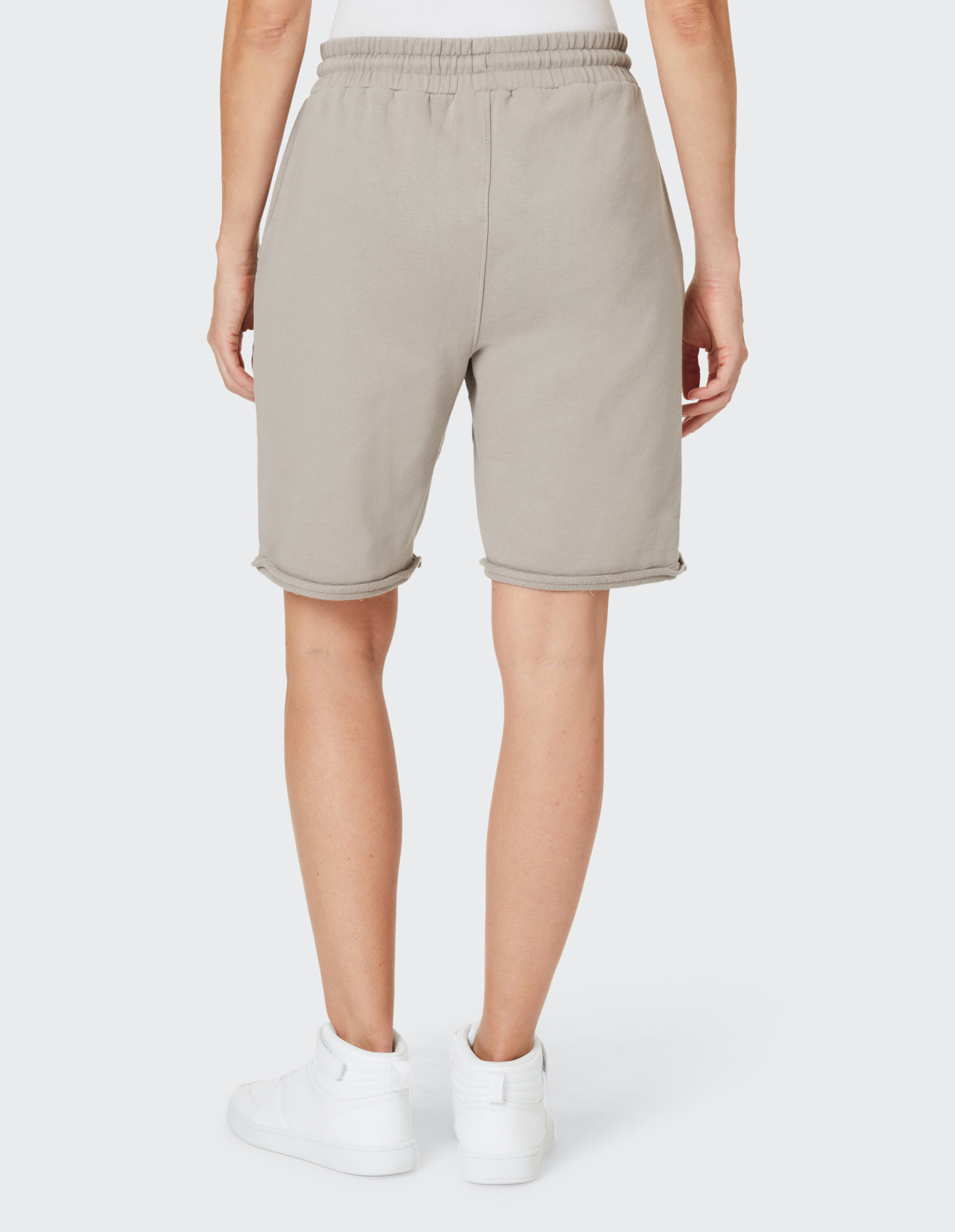 Rückansicht einer Frau, die beige Freizeitshorts und weiße Turnschuhe trägt.