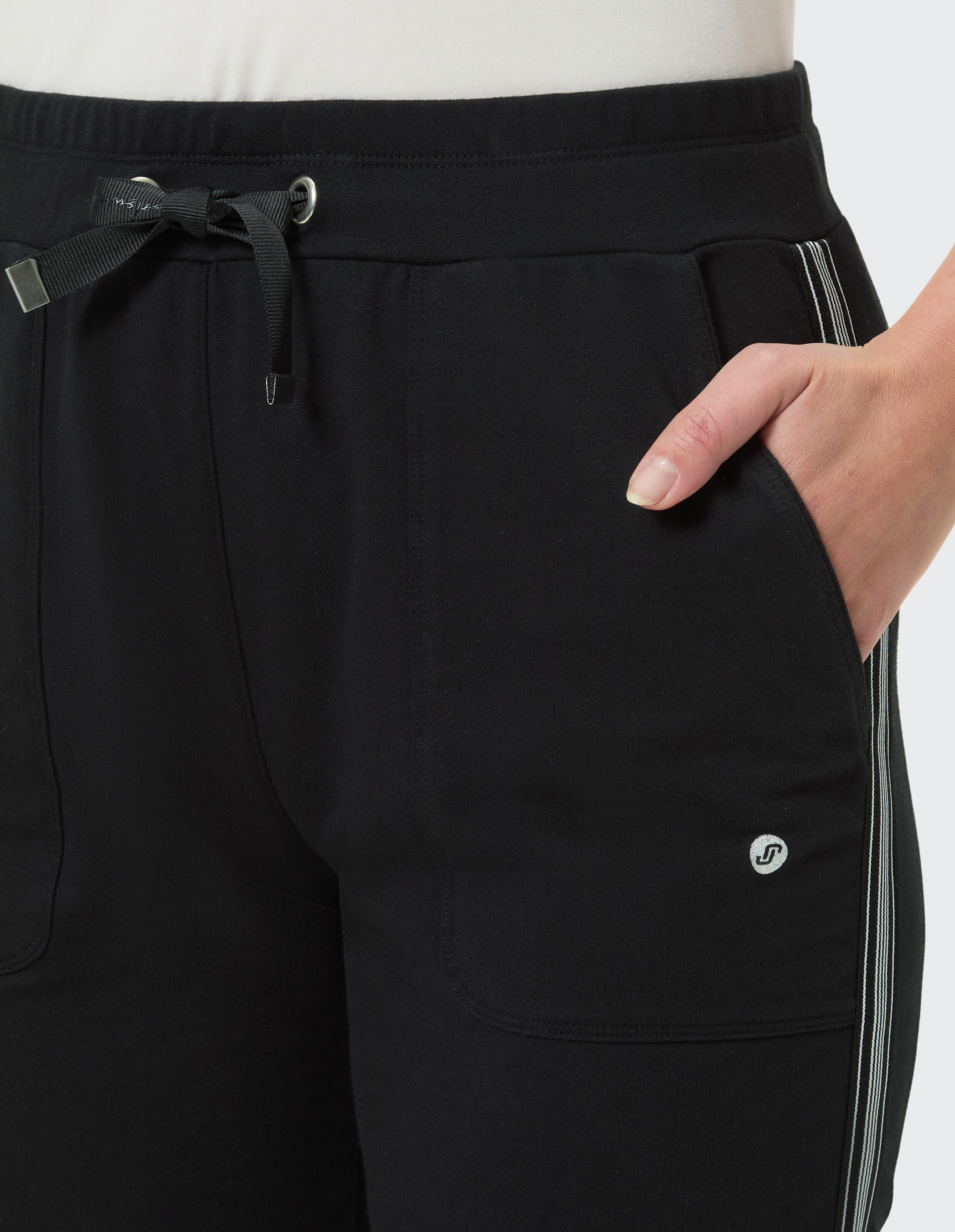 Schwarze Hose mit Streifen an der Seite und Kordelzug, die mit der Hand in der Tasche getragen wird.