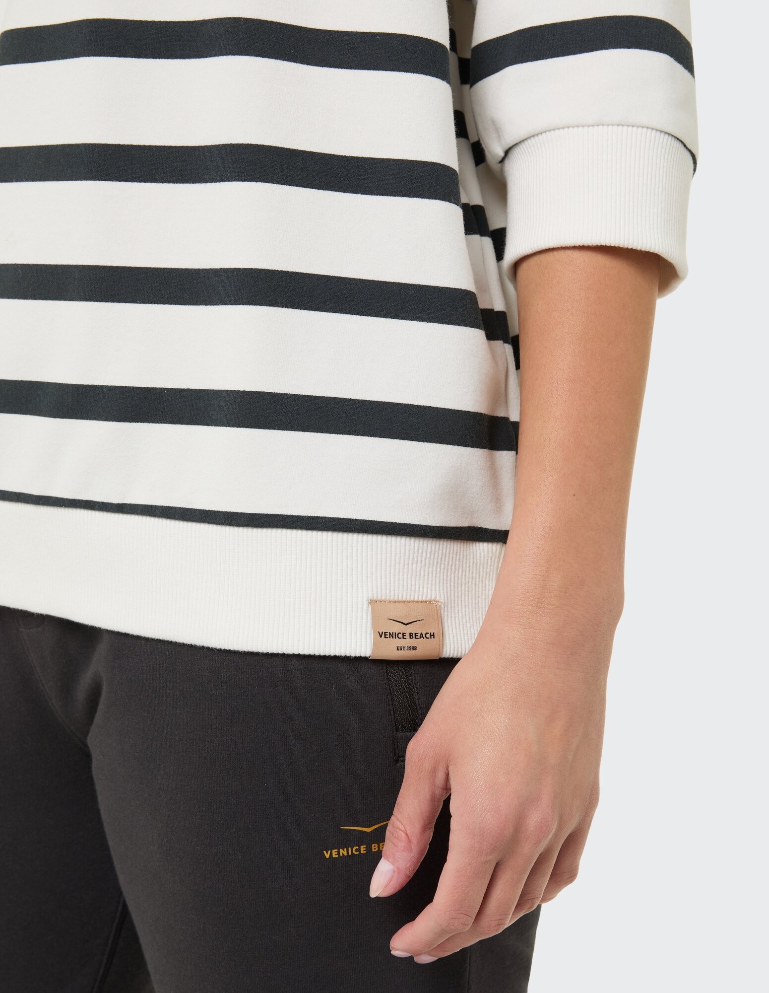 Nahaufnahme eines gestreiften weiß-schwarzen Pullovers mit Venice Beach-Label und einer dunklen Hose.