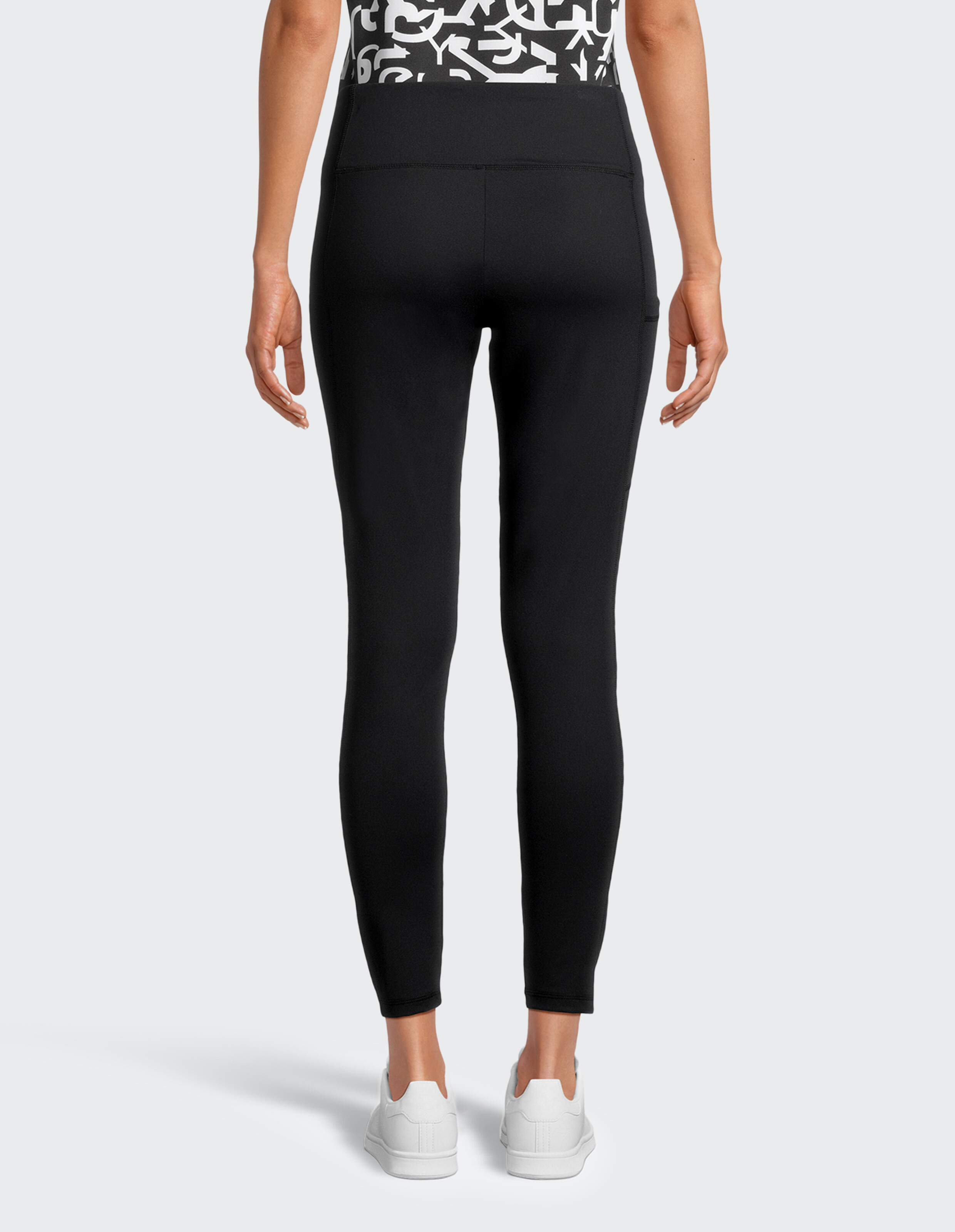 Rückansicht einer schwarzen lässigen Leggings mit hohem Bund und weißen Turnschuhen.