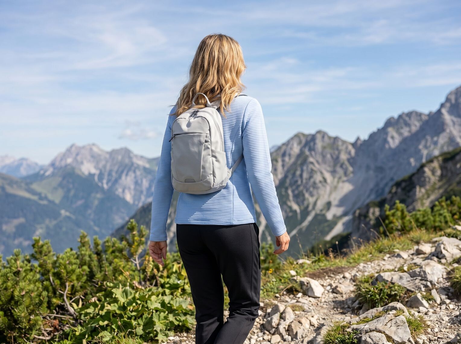 Frau in einem hellblauen Oberteil und einer schwarzen Hose wandert in den Bergen.