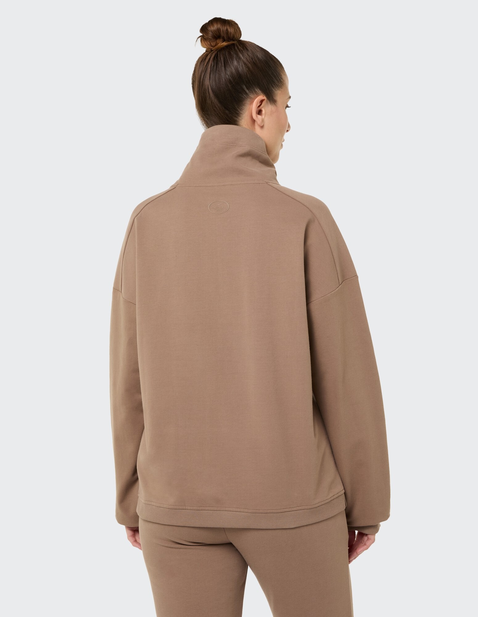 Rückansicht einer Frau in einem kuscheligen braunen Pullover, perfekt für Freizeitkleidung.