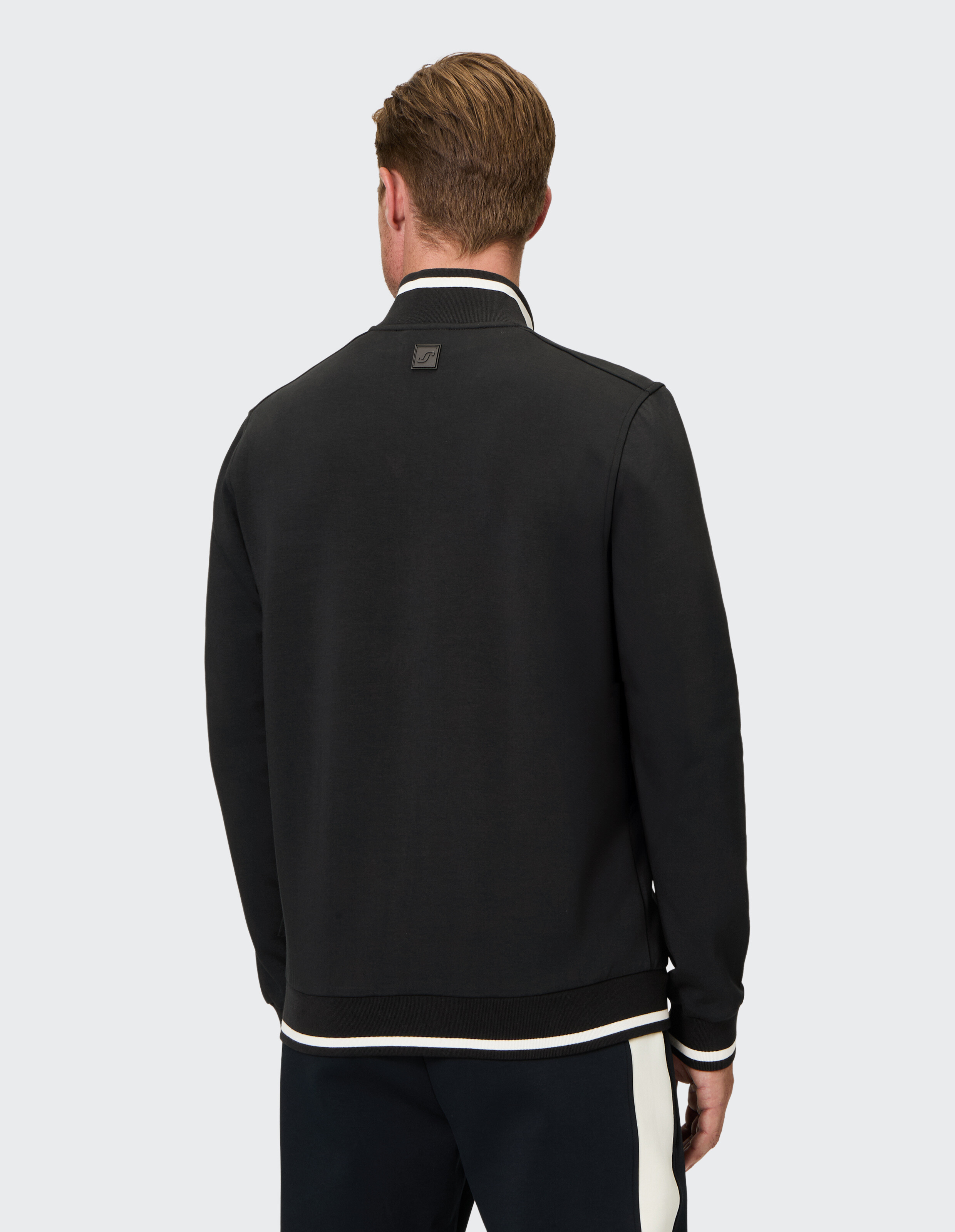Rückansicht eines Mannes, der eine schwarze Freizeitjacke mit weißem Besatz trägt.