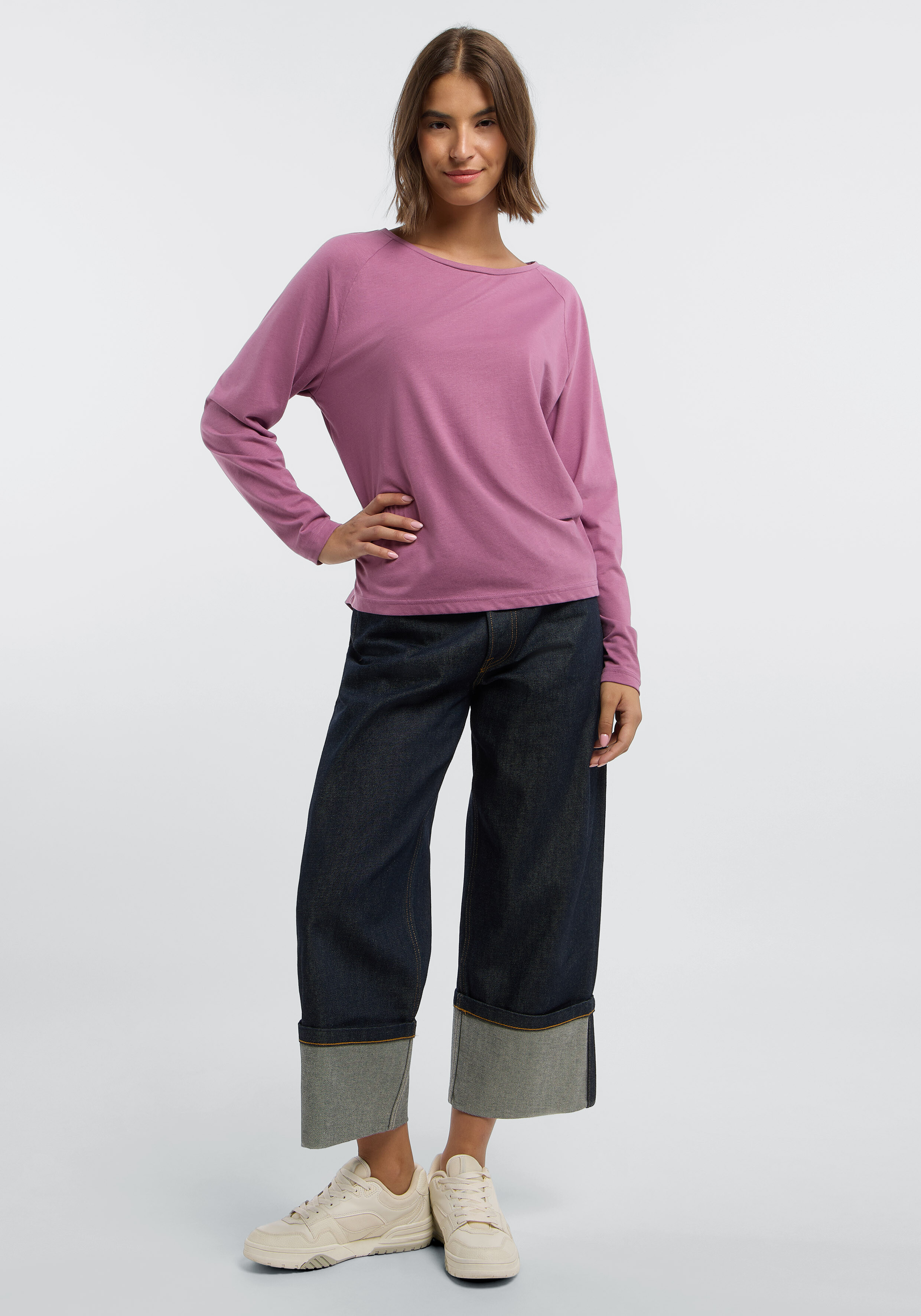 Frau trägt ein gemütliches lilafarbenes Langarmhemd und Jeans mit weitem Bein.