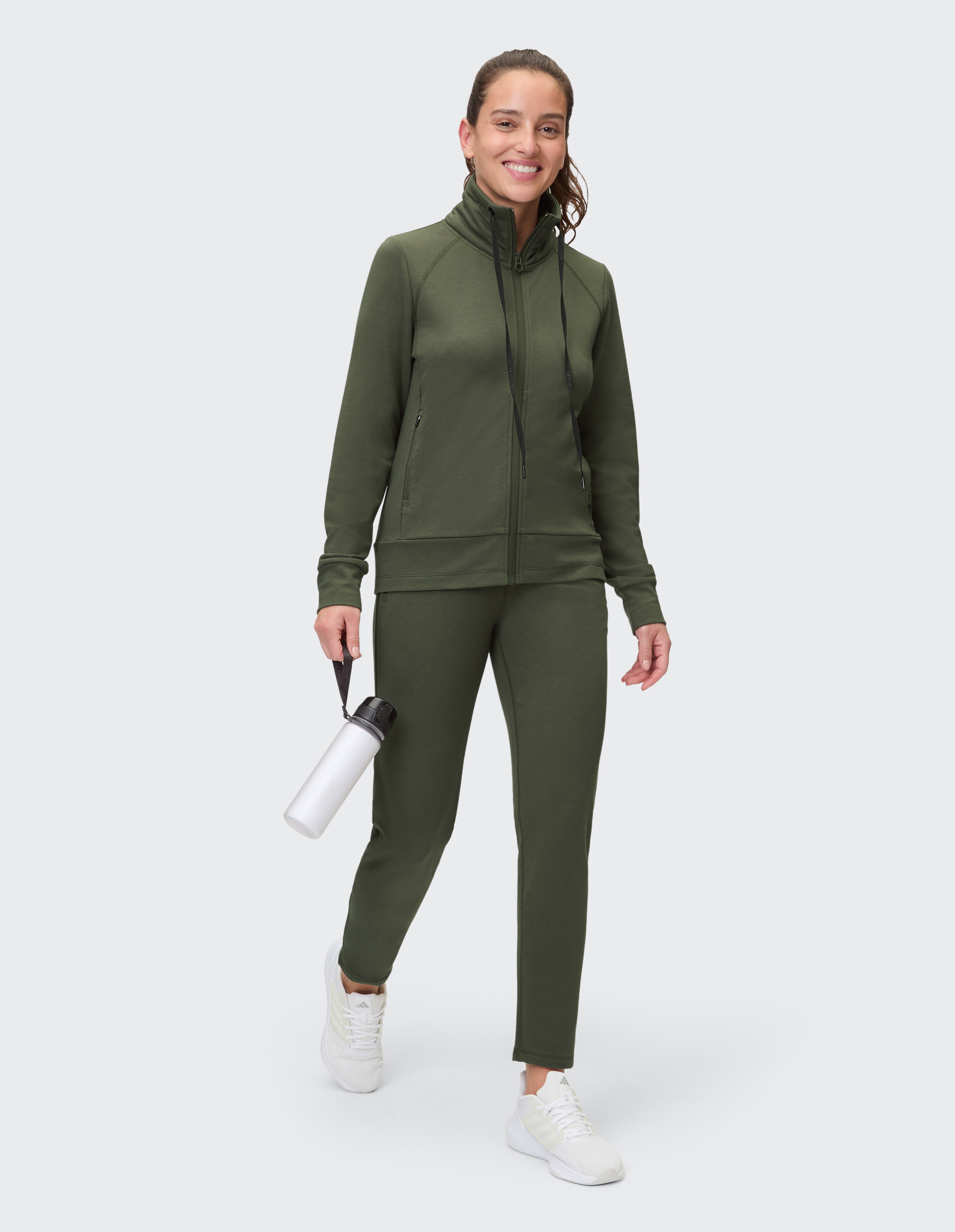 Frau trägt ein gemütliches olivgrünes Lounge-Set mit einer Jacke mit Reißverschluss und passender Hose.
