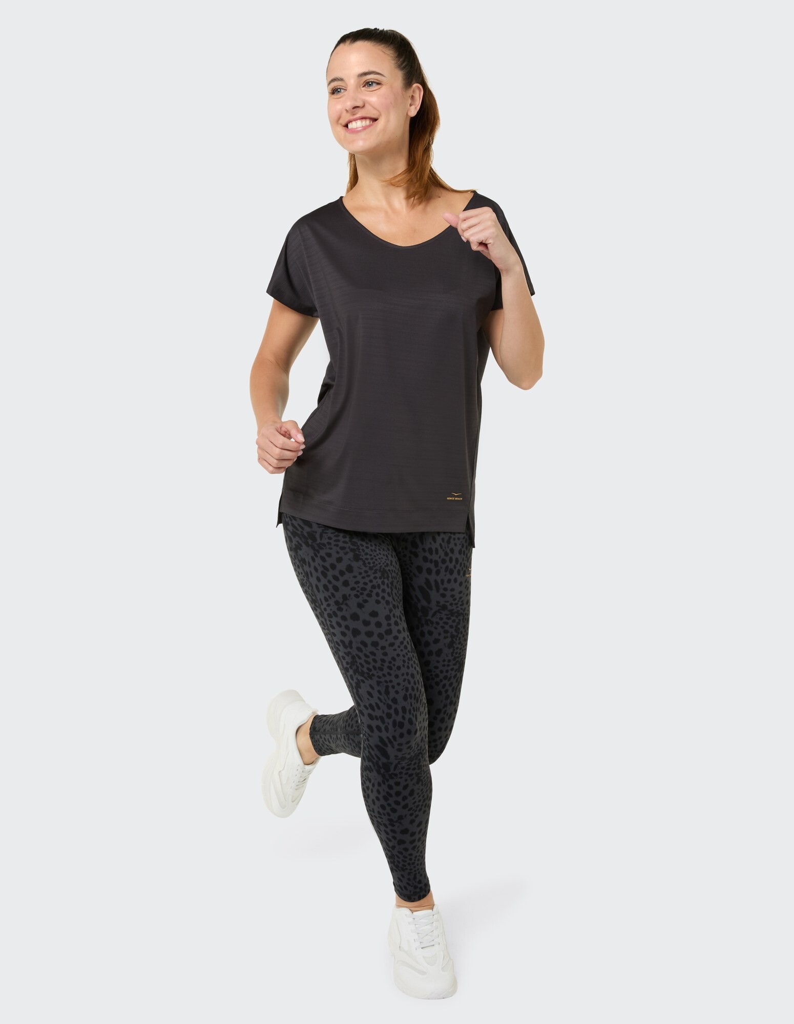 Frau in schwarzem Freizeitoberteil und Leggings mit Leopardenmuster, lächelnd und posierend.