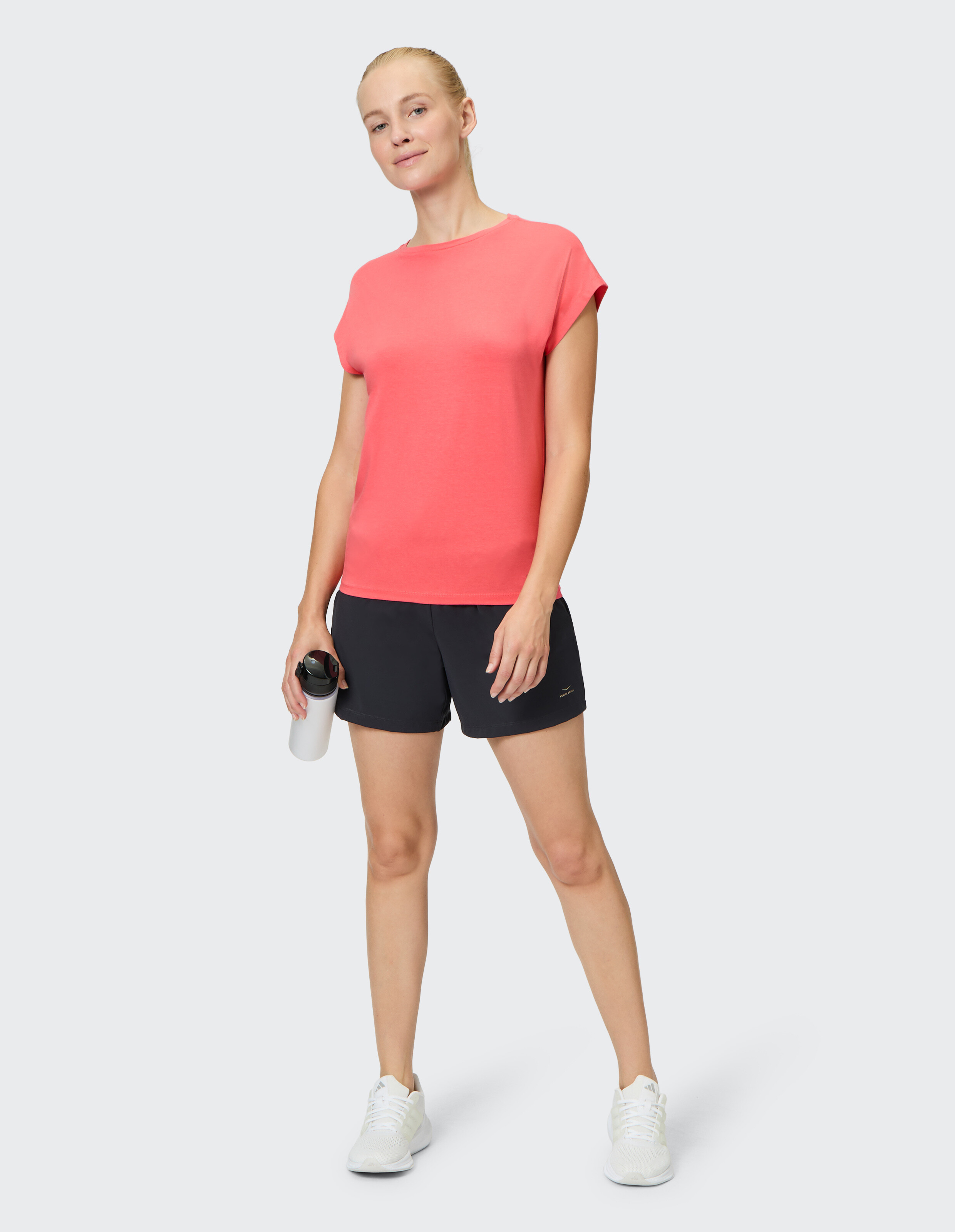 Frau trägt ein korallenrotes Venice Beach Kurzarmshirt Yvi und schwarze Shorts.