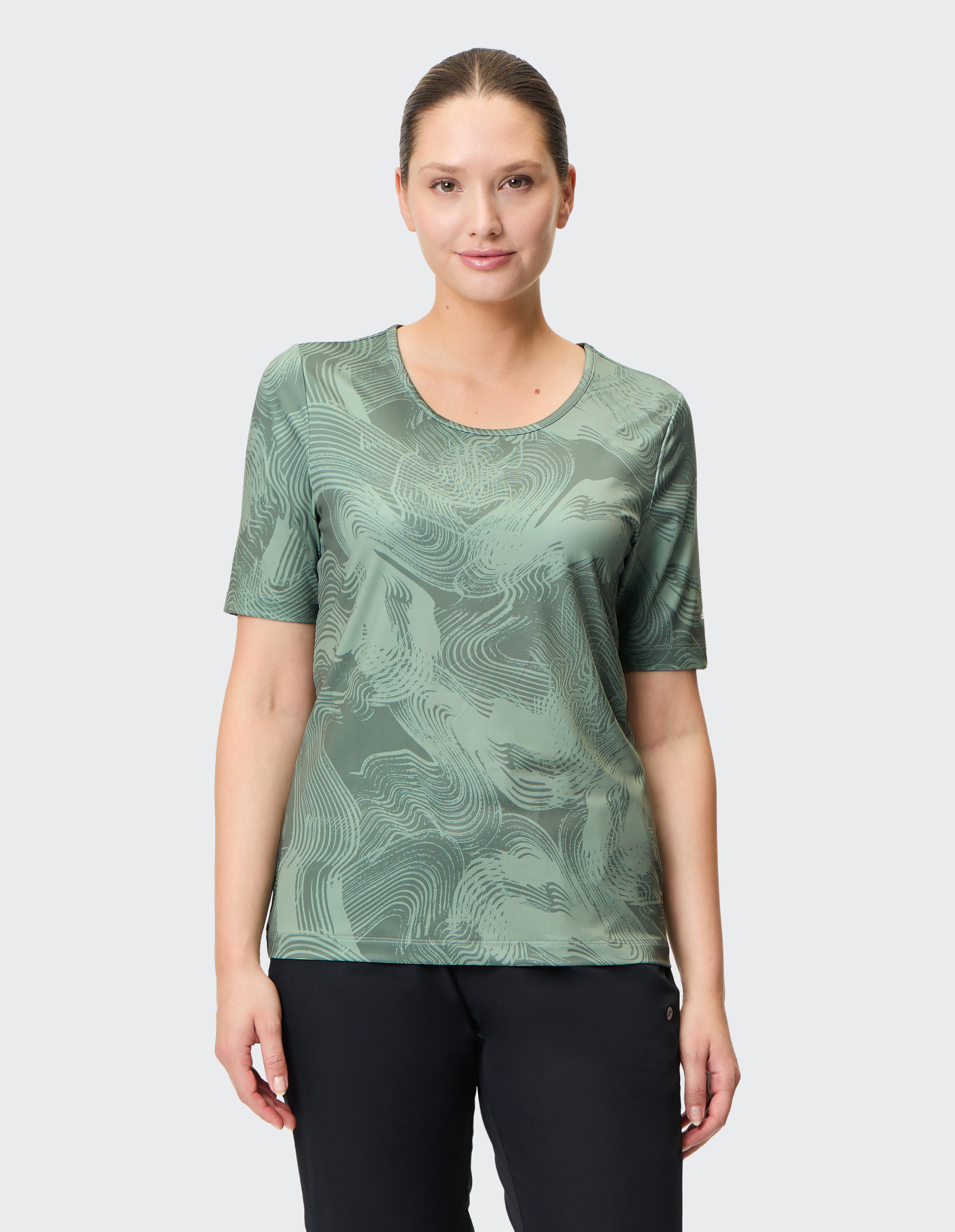 Frau trägt ein grün gemustertes Freizeit-T-Shirt mit rundem Ausschnitt.