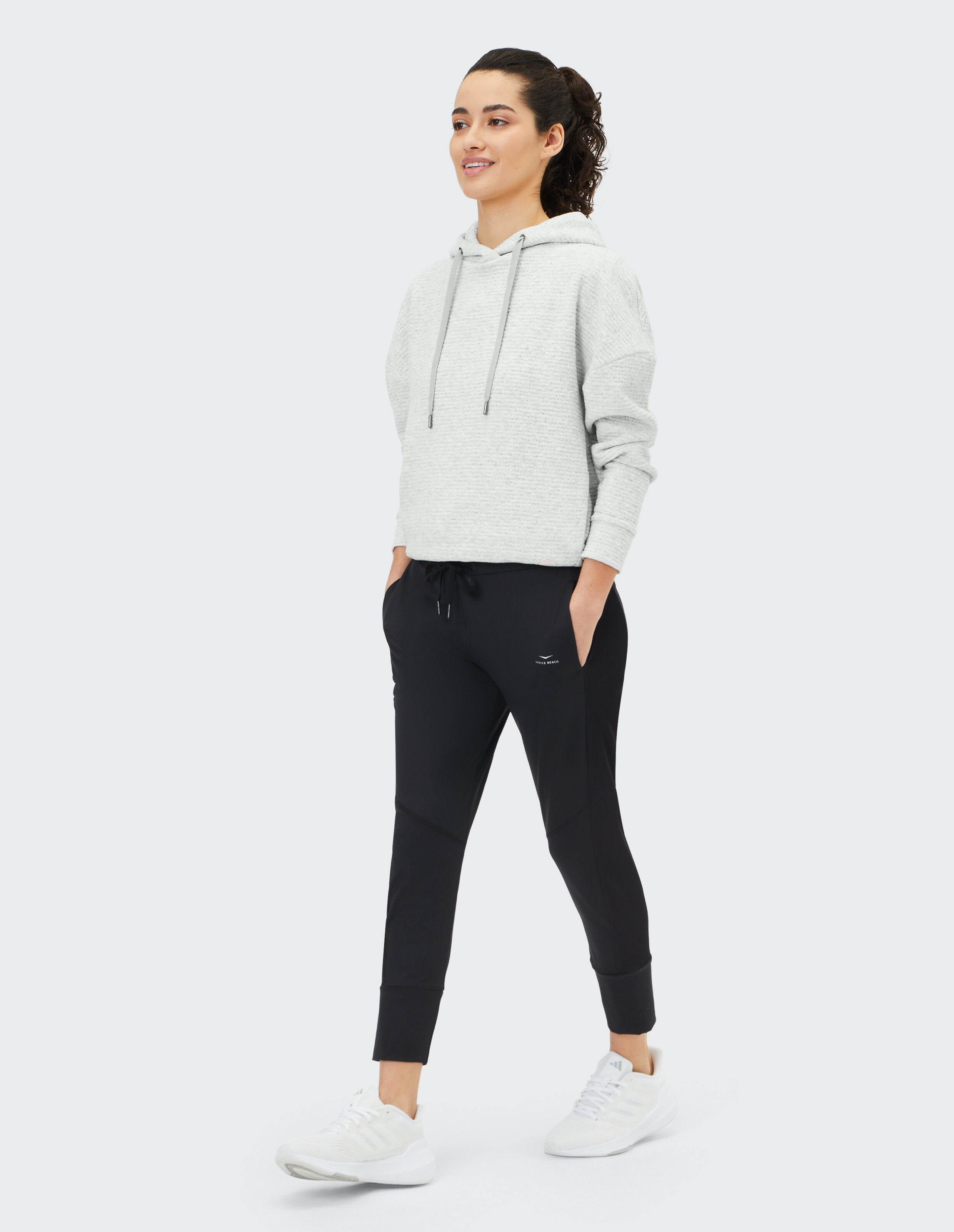 Frau trägt einen kuscheligen, grauen, strukturierten Kapuzenpullover und eine schwarze Lounge-Hose für einen lässigen Stil.