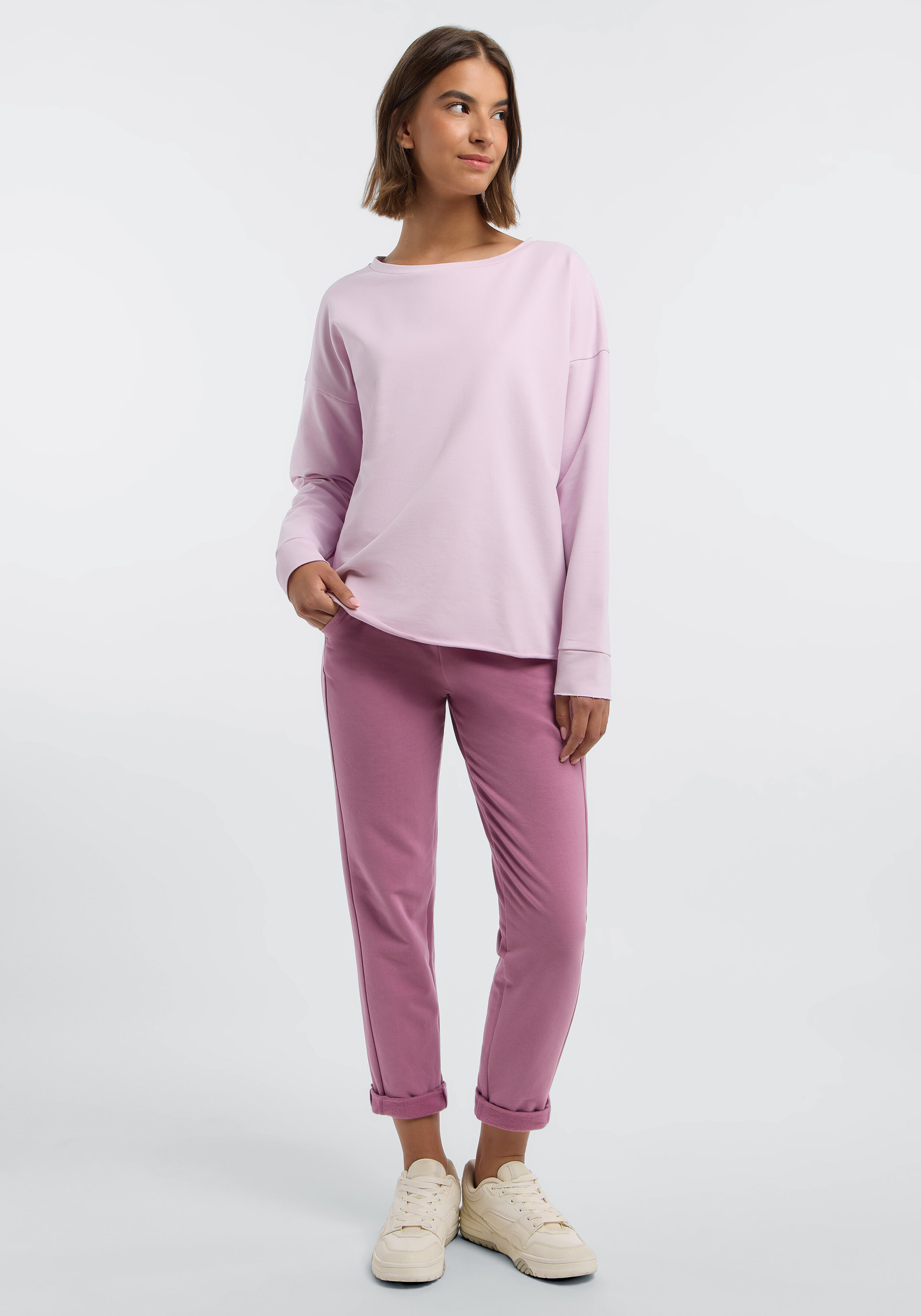 Frau trägt ein hellrosa Langarmshirt und eine malvenfarbene Freizeithose.