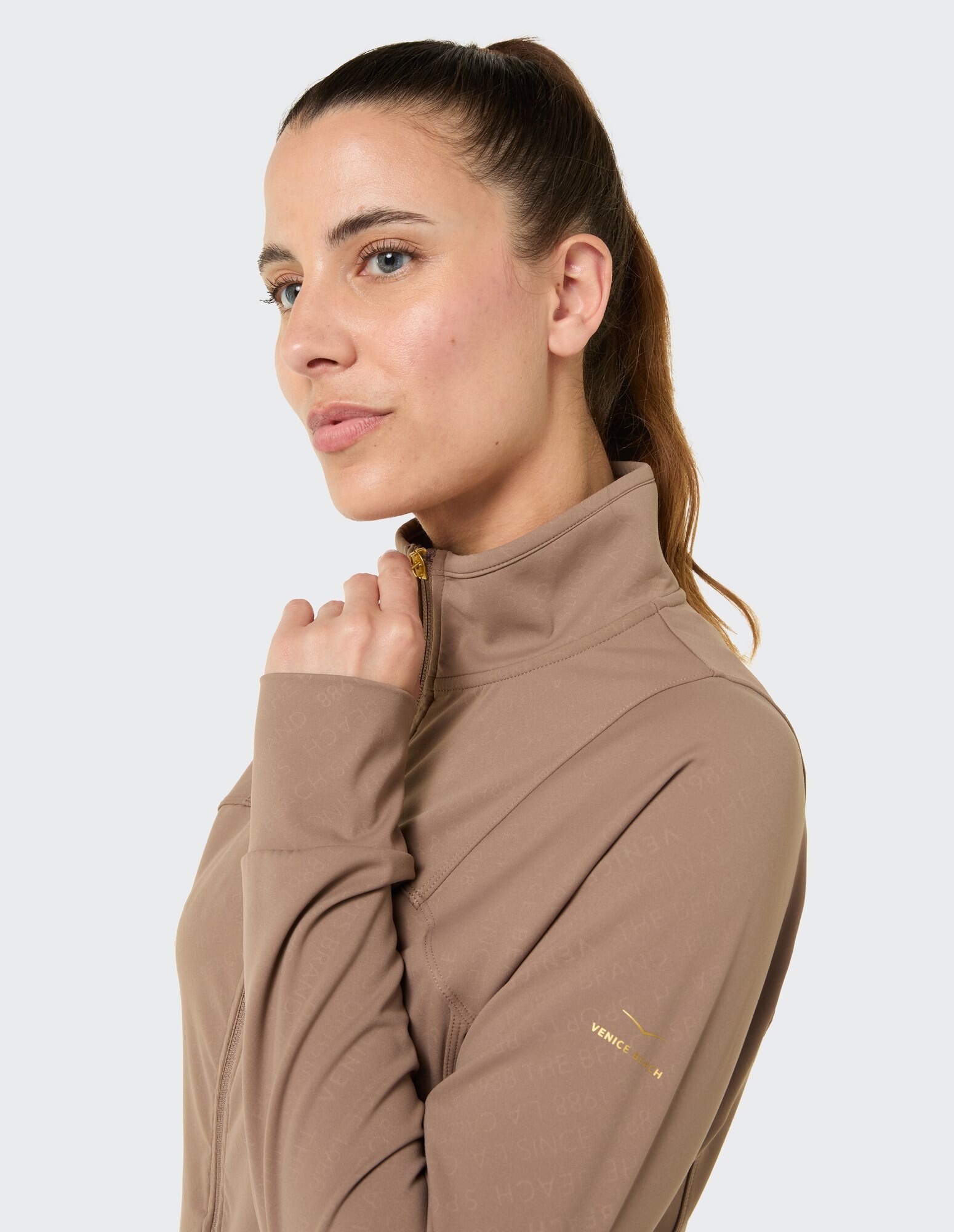 Nahaufnahme einer Frau in einer beigen Jacke mit Reißverschluss, die einen lässigen und stilvollen Look zeigt.
