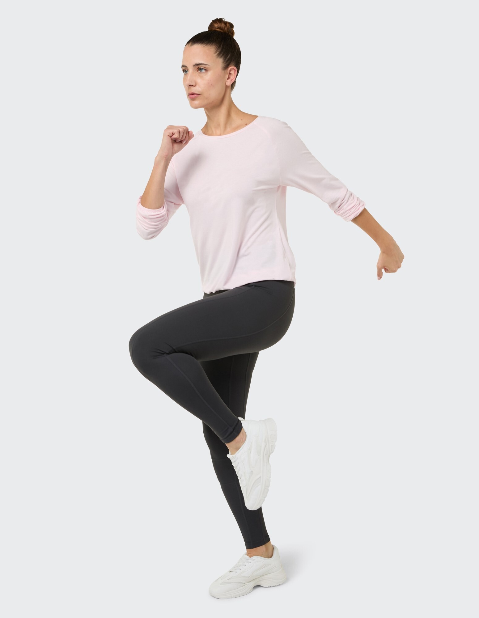Modell in einem hellrosa Langarm-Top und schwarzen Leggings, gestylt für Freizeitkleidung.
