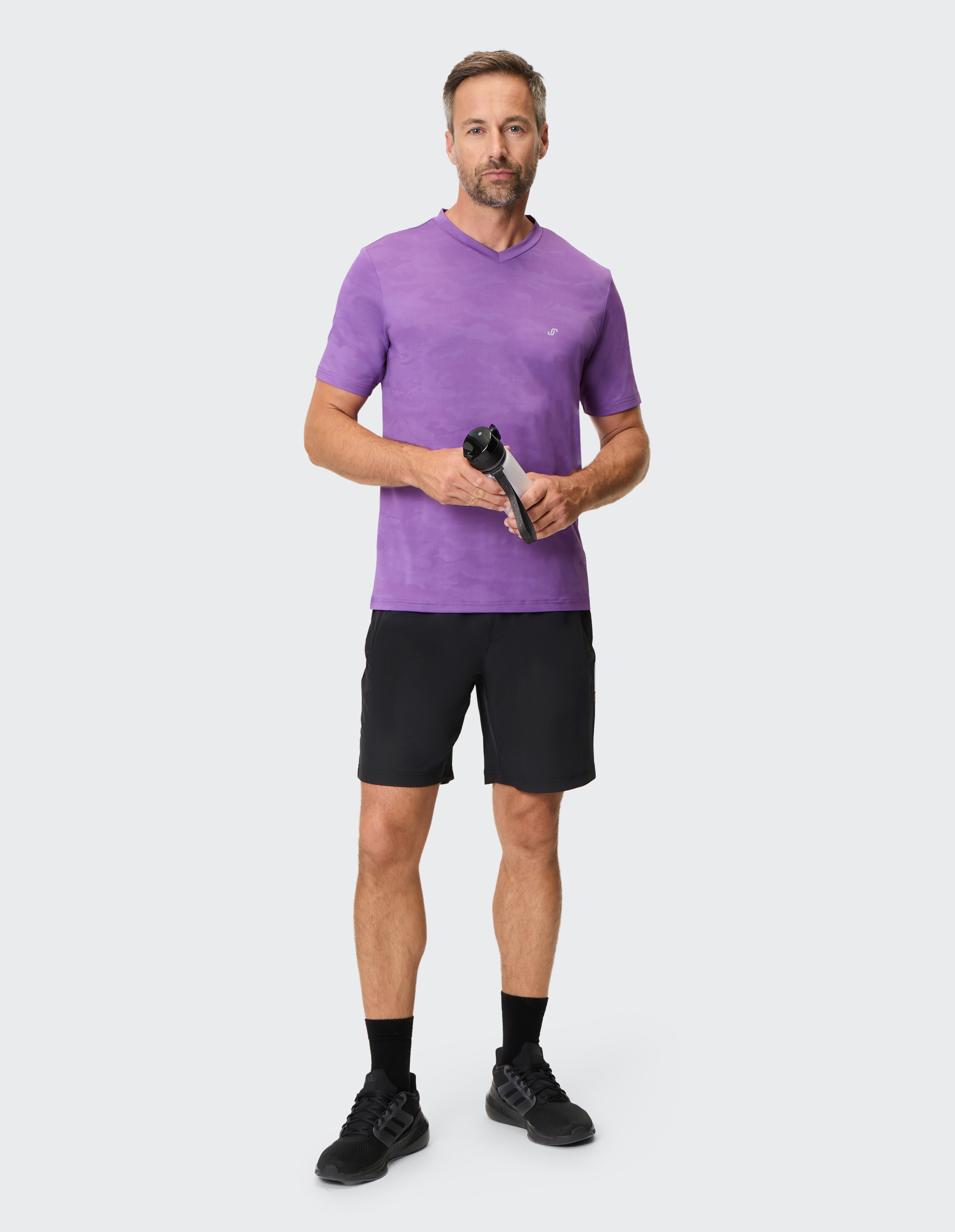 Mann trägt ein lila T-Shirt mit V-Ausschnitt und schwarze Shorts für einen lässigen, sportlichen Look.
