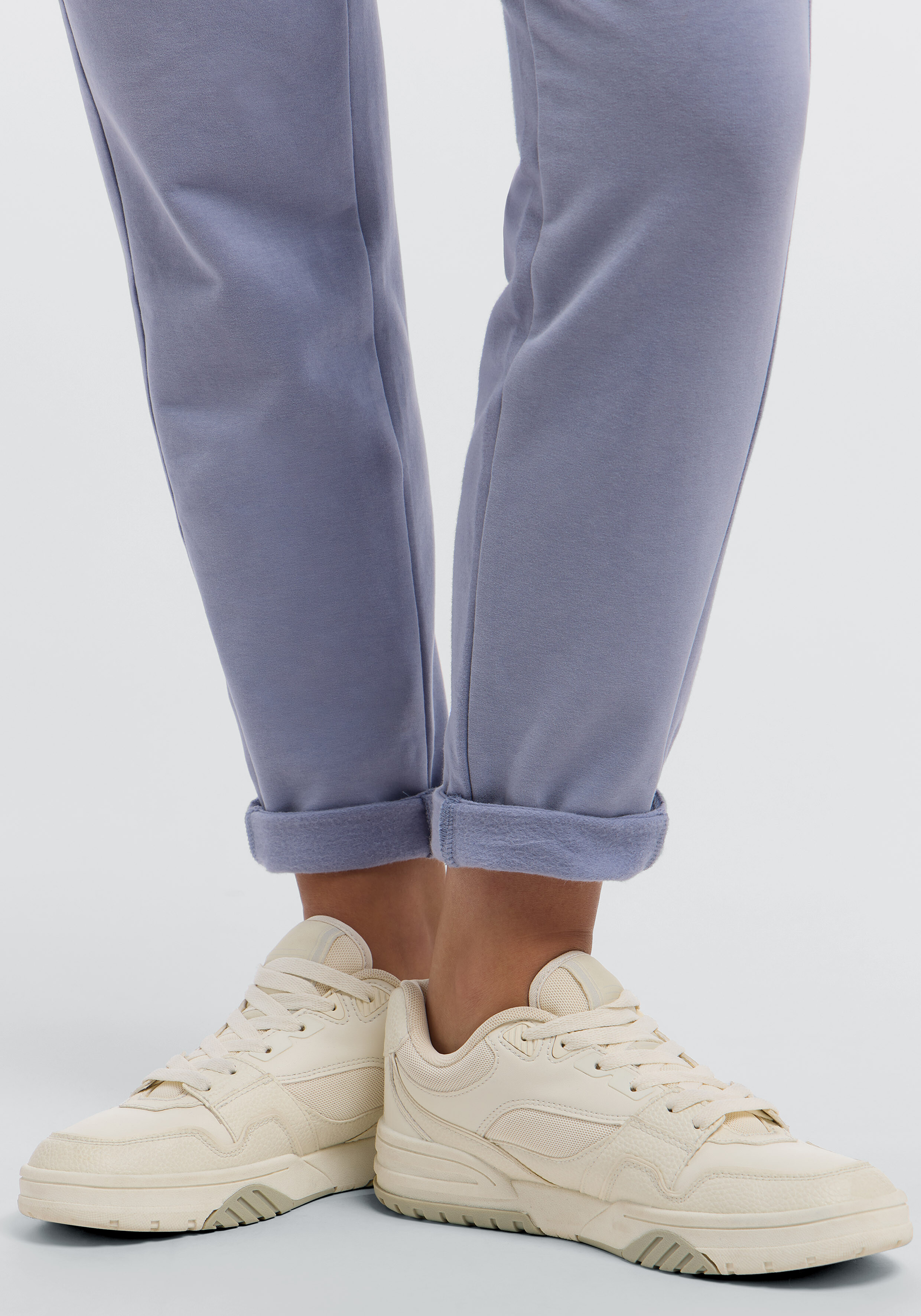 Nahaufnahme einer hellblauen Freizeit-Jogginghose mit Bündchen am Saum und cremefarbenen Turnschuhen.