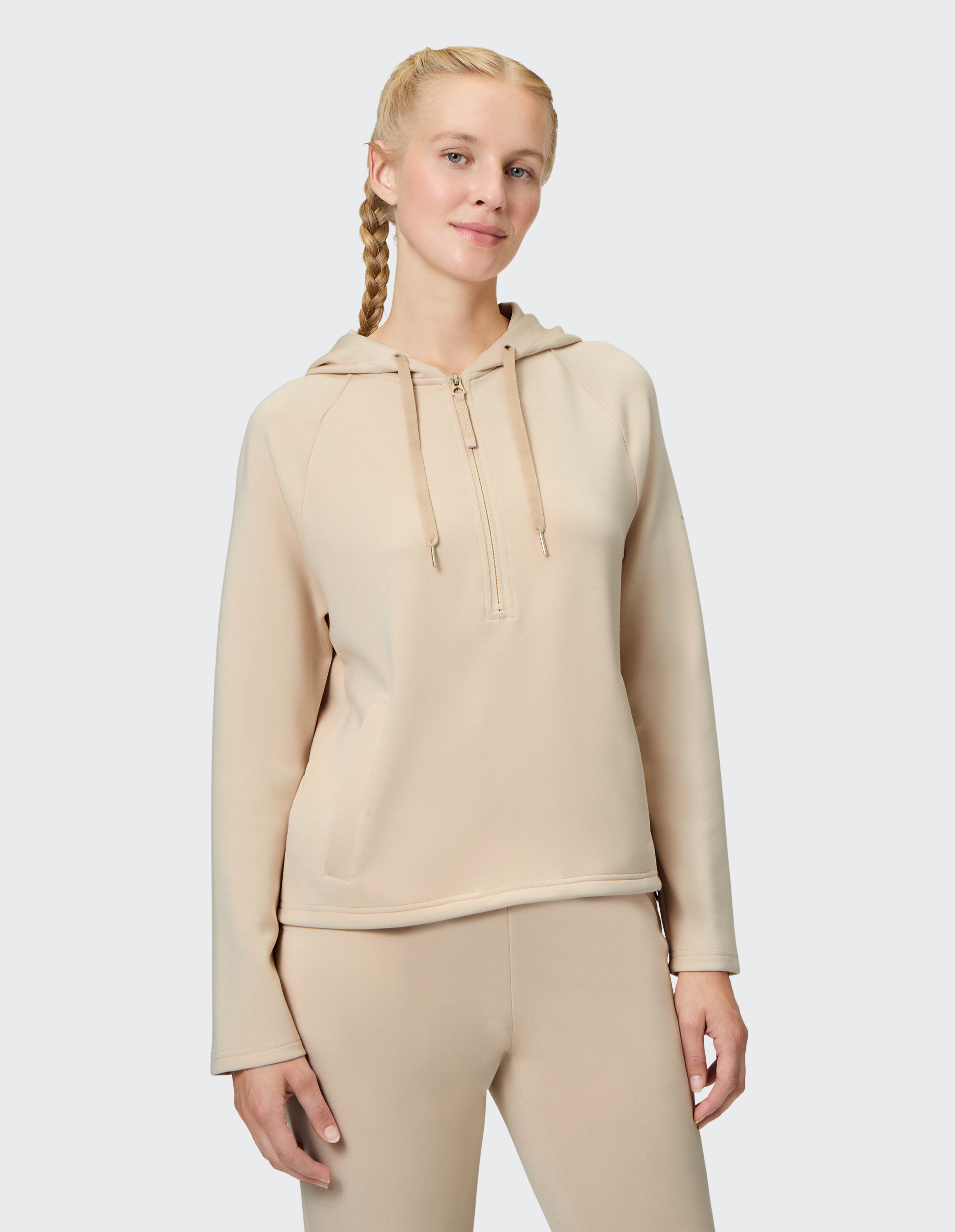 Frau trägt einen beigen Kapuzenpullover mit halbem Reißverschluss für gemütliche, lässige Loungewear.