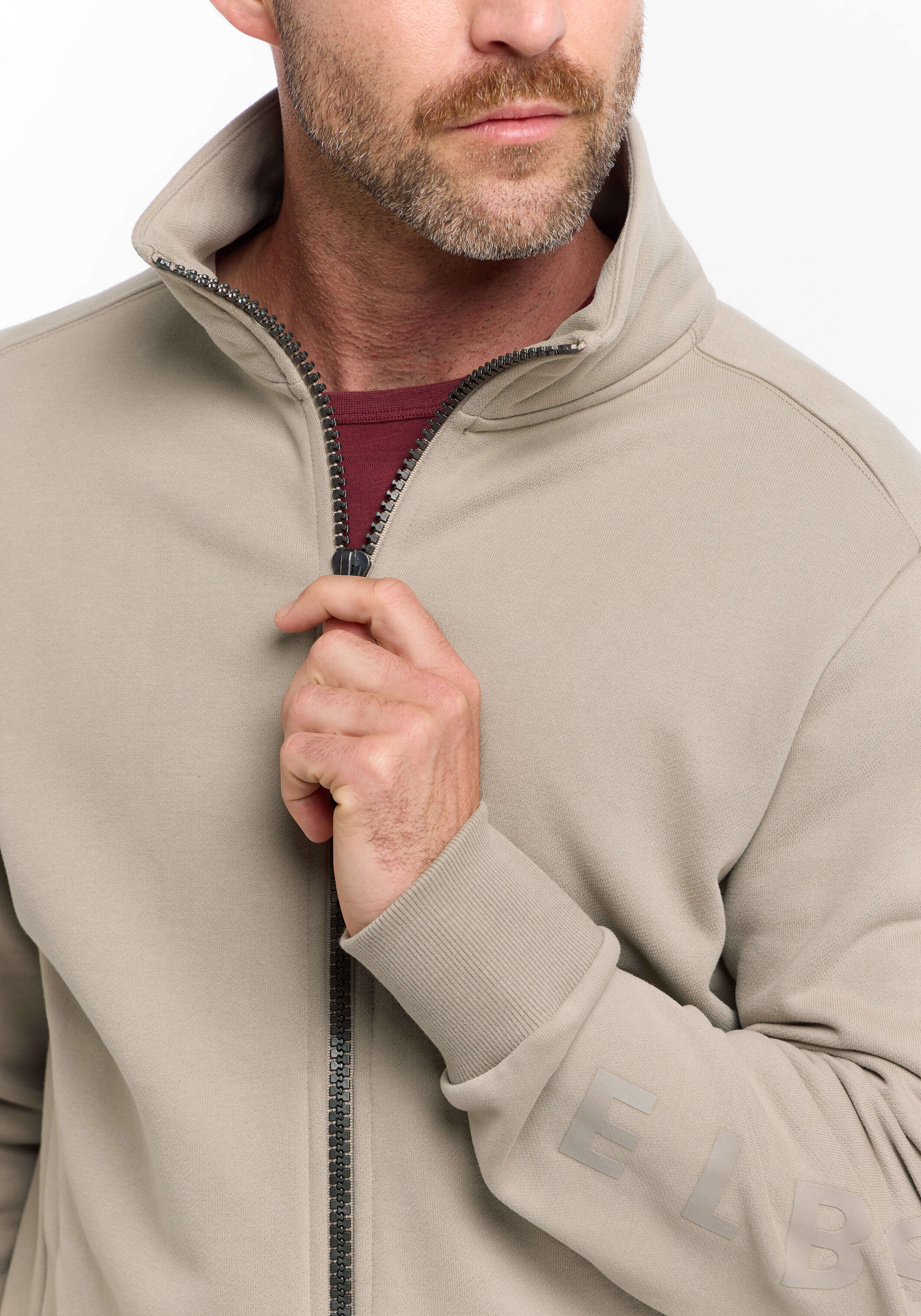 Mann trägt ein beiges ELBSAND-Sweatshirt mit Reißverschluss und gerippten Bündchen für lässigen Komfort.
