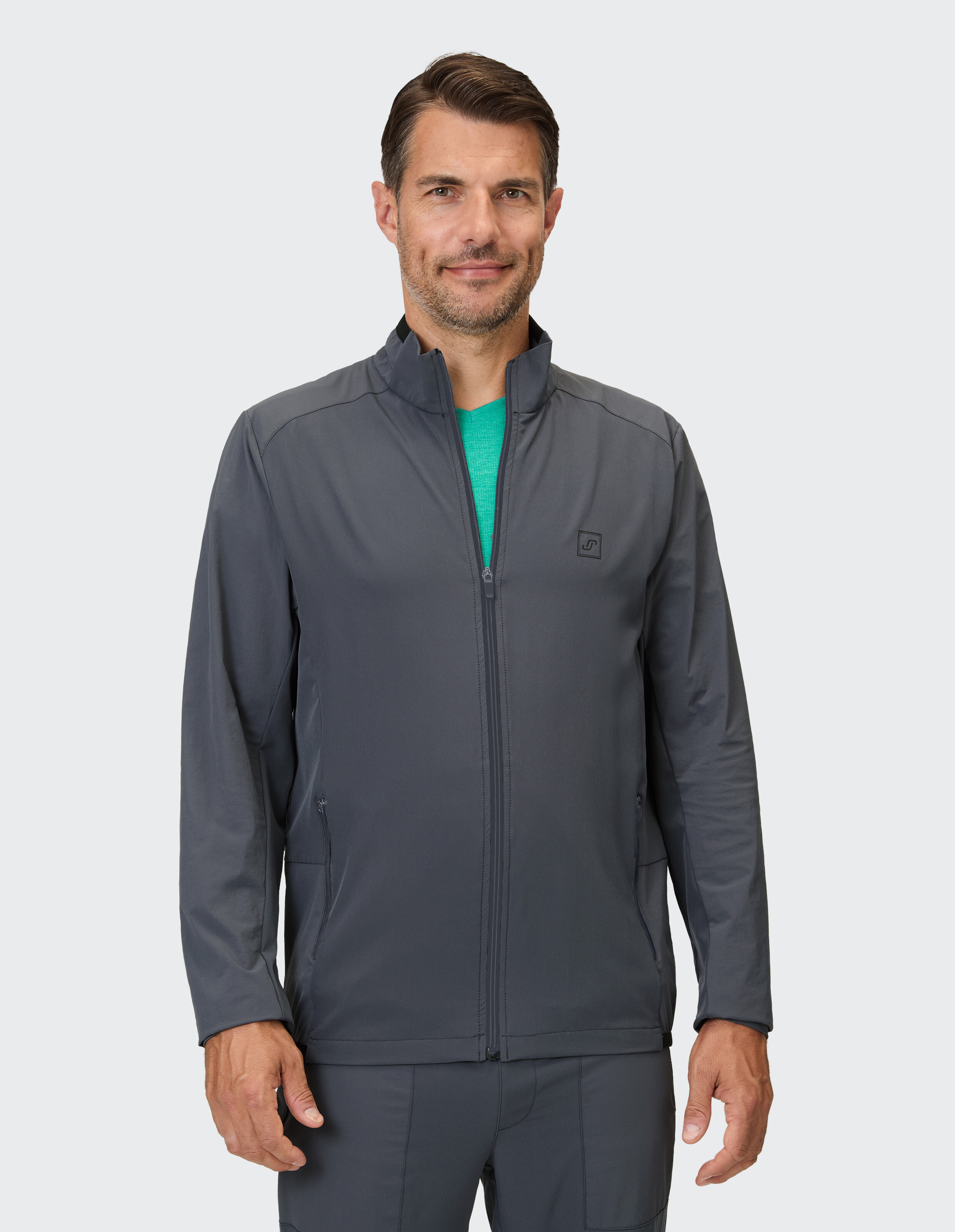 Ein Mann trägt eine dunkelgraue Reißverschlussjacke mit Stehkragen und einen grünen Pullover darunter.