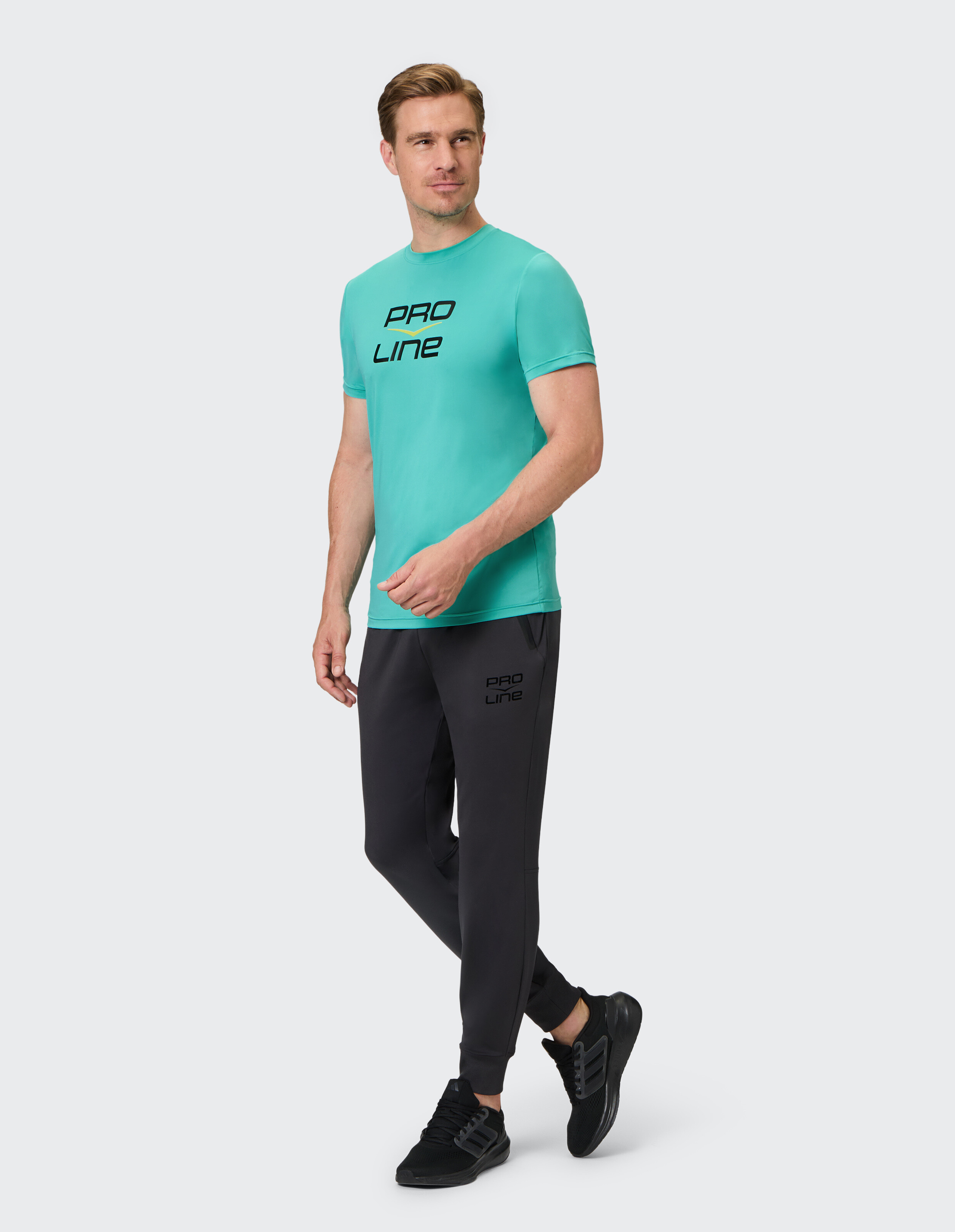 Mann im türkisfarbenen PRO LINE T-Shirt und schwarzen Jogginghosen, stilvolle Freizeitkleidung.