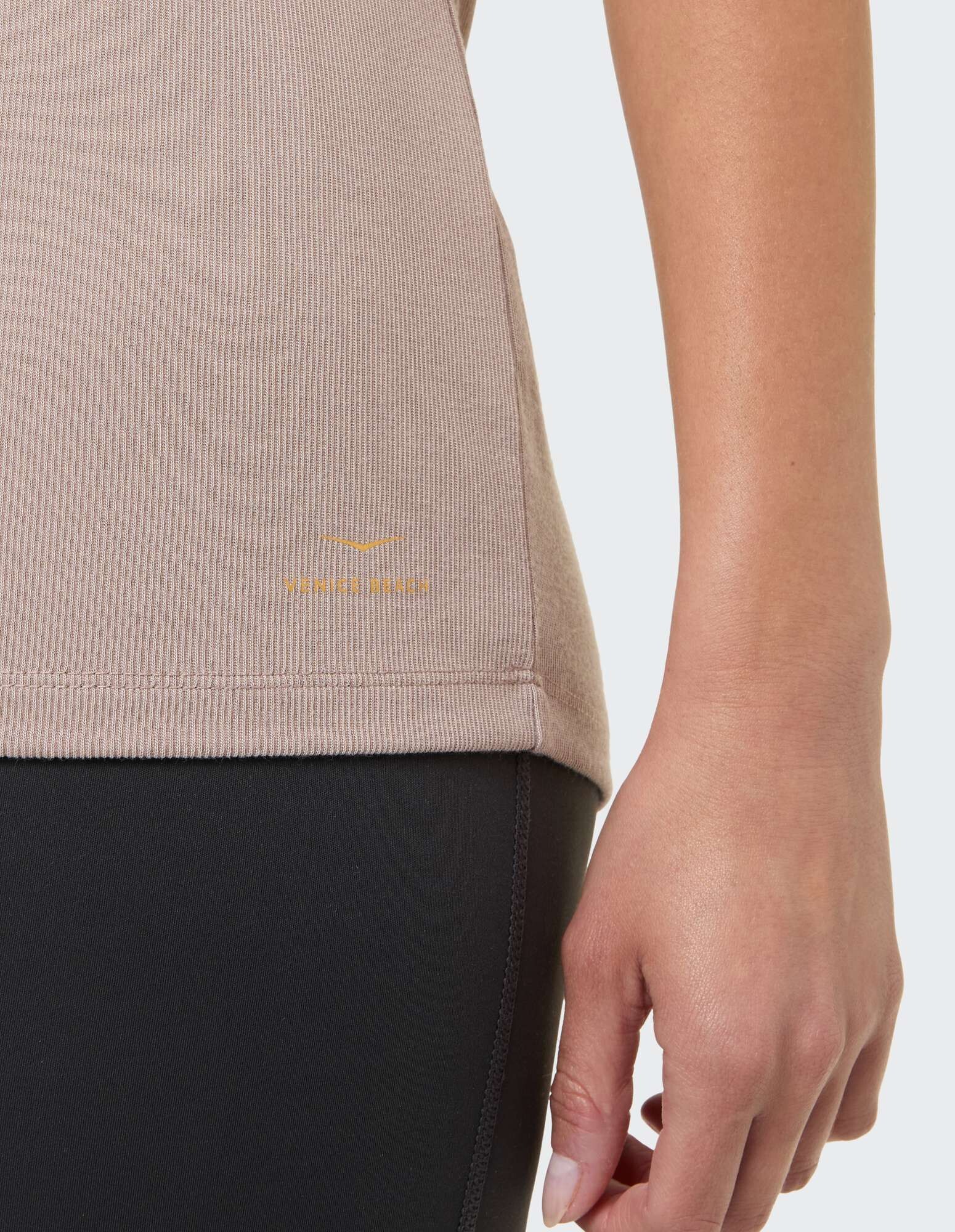 Nahaufnahme eines beigen gerippten Oberteils gepaart mit schwarzen Leggings, die für Komfort sorgen.