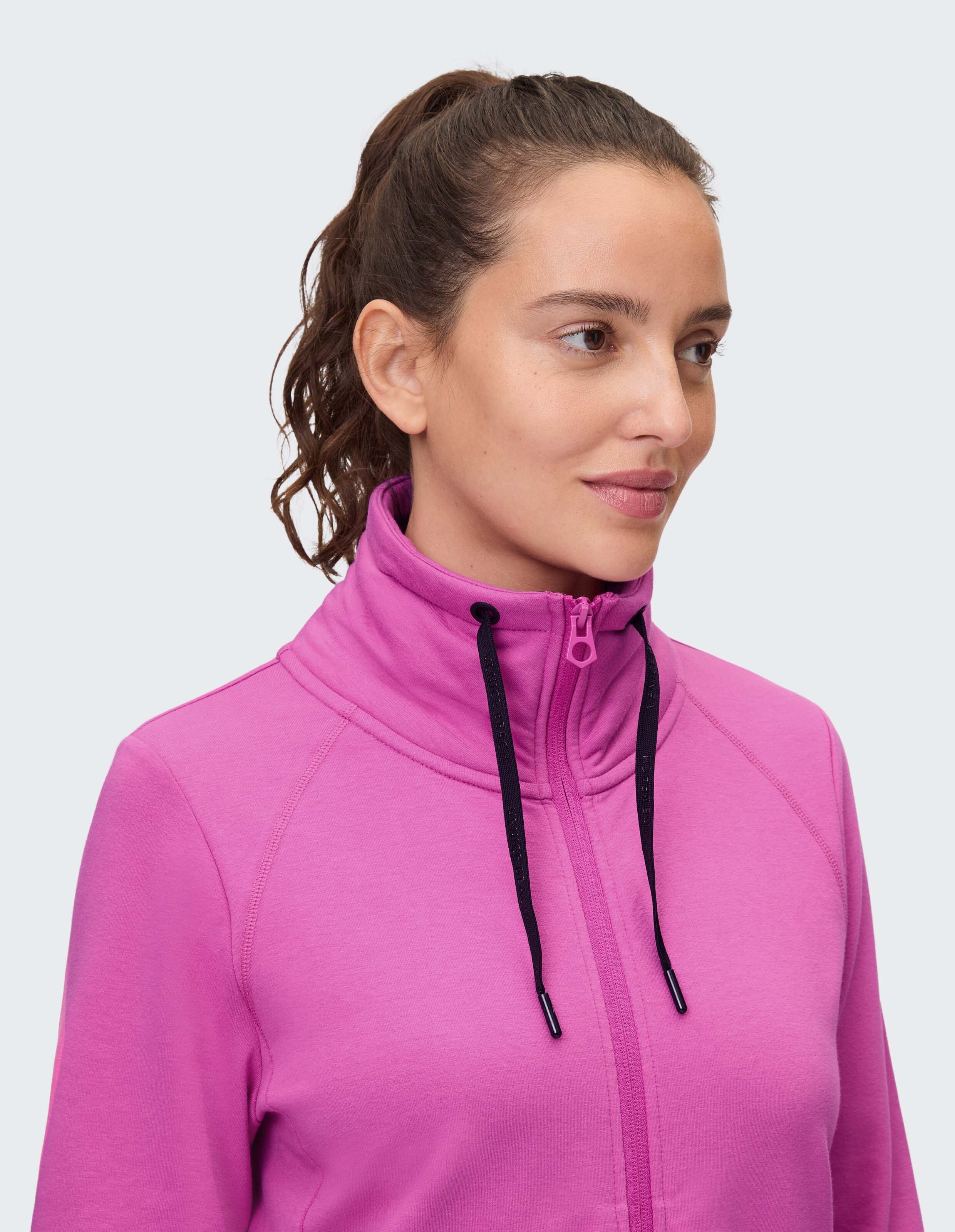Nahaufnahme einer Frau in einem rosa Kapuzenpullover mit Reißverschluss, hohem Kragen und Kordelzug.