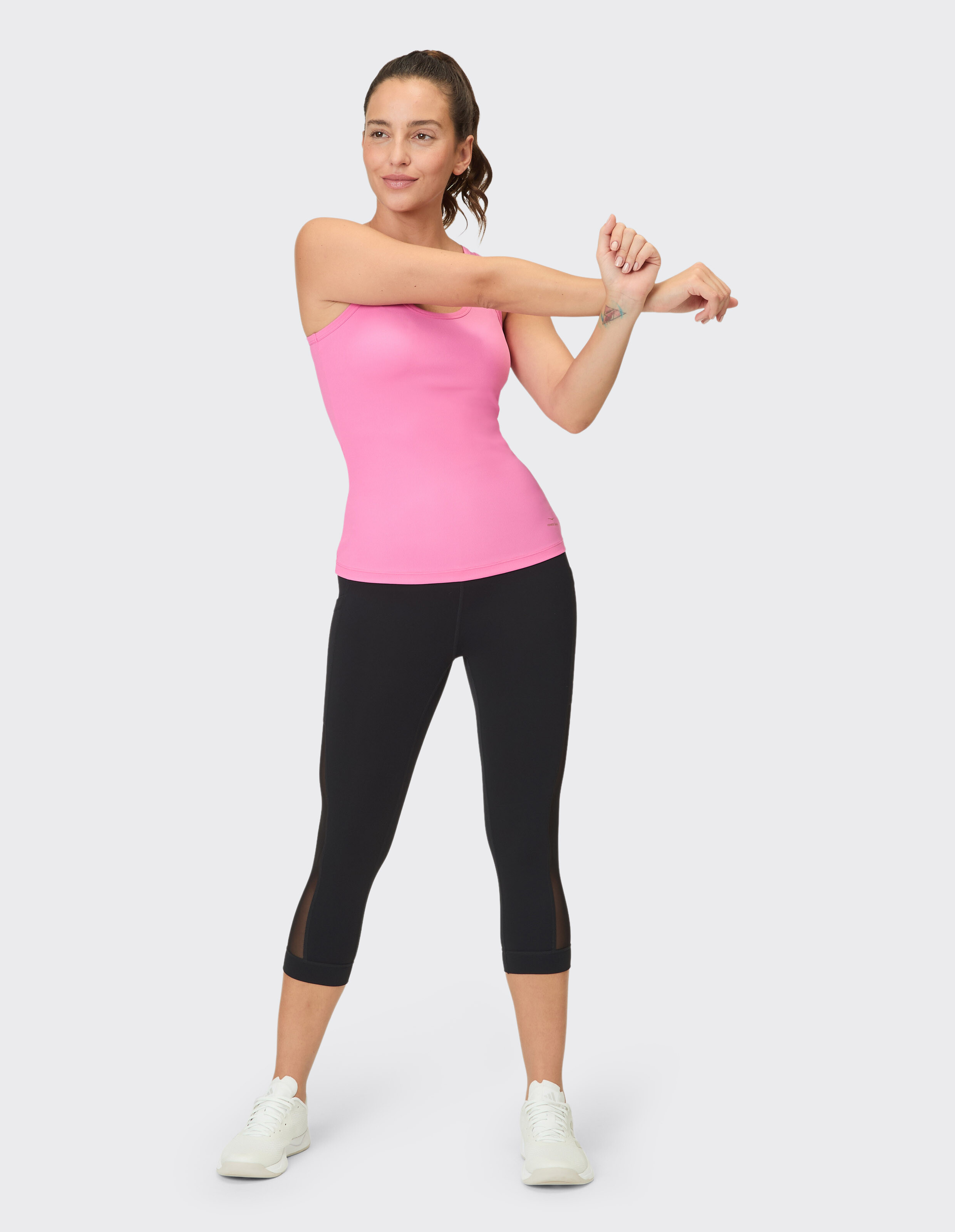 Frau in rosafarbenem Tanktop und schwarzen Capri-Leggings dehnt sich in lässiger Atmosphäre.