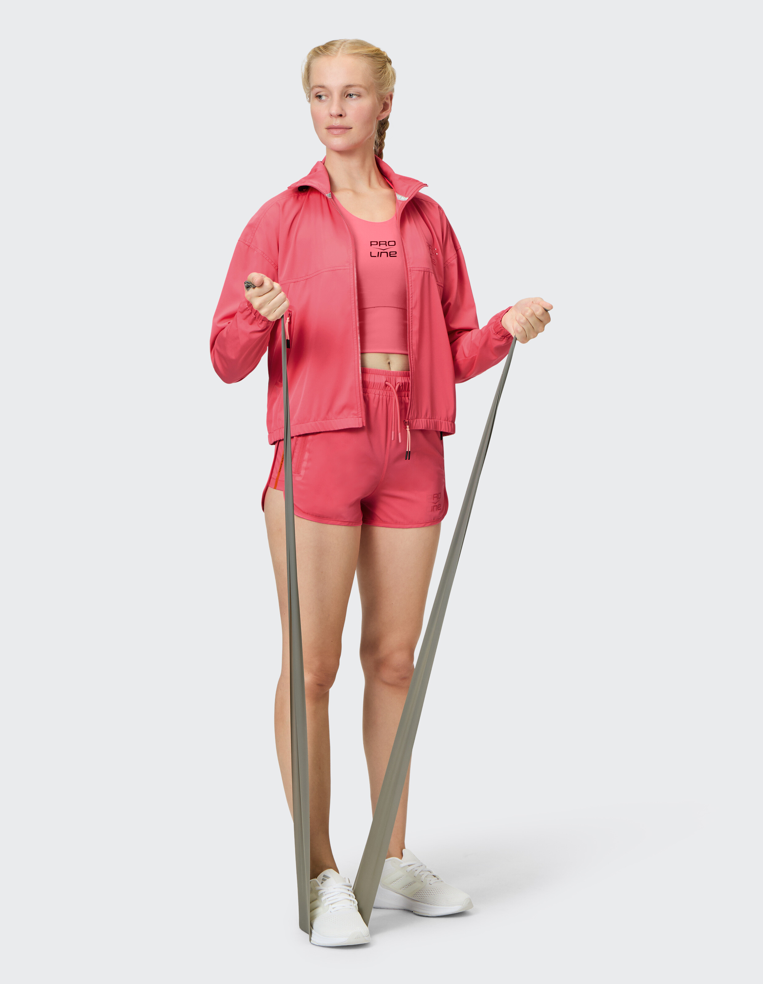Frau in rosa Sportkleidung mit Jacke und Shorts trainiert mit Widerstandsbändern.
