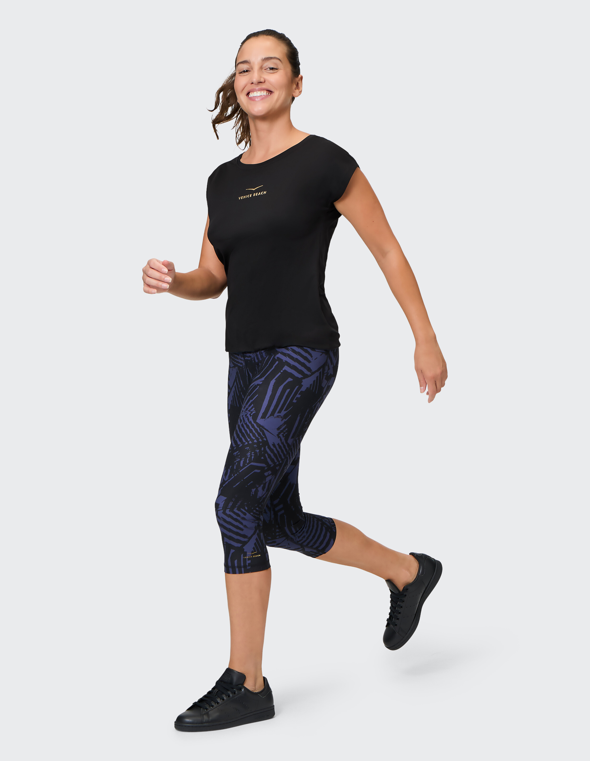 Frau trägt ein schwarzes T-Shirt und gemusterte Capri-Leggings für lässige Aktivkleidung.