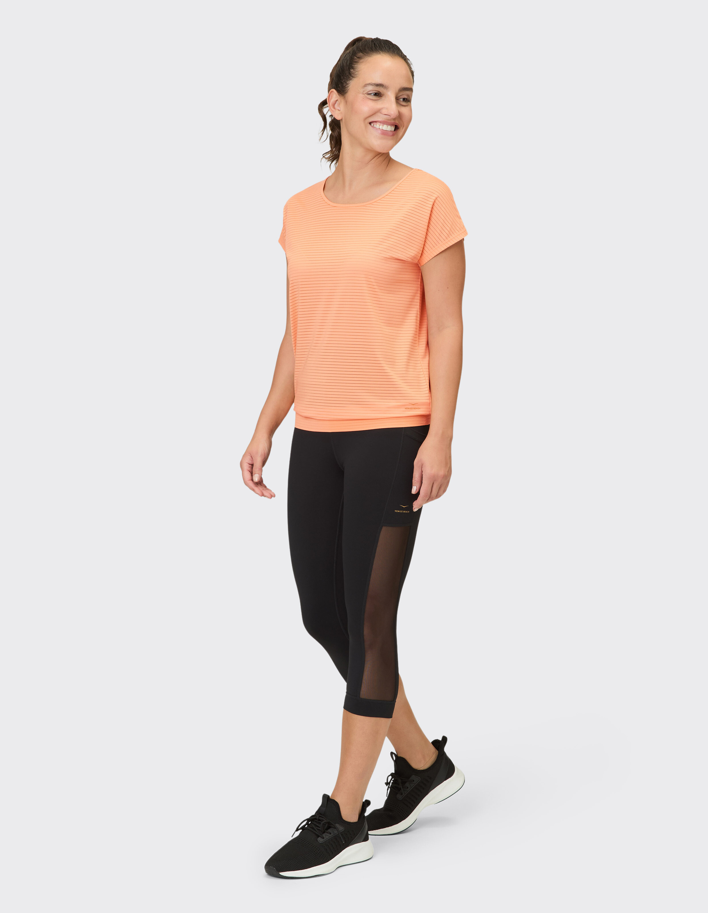 Frau in einem pfirsichfarbenen, gestreiften Oberteil und schwarzen Capri-Leggings, die selbstbewusst geht.