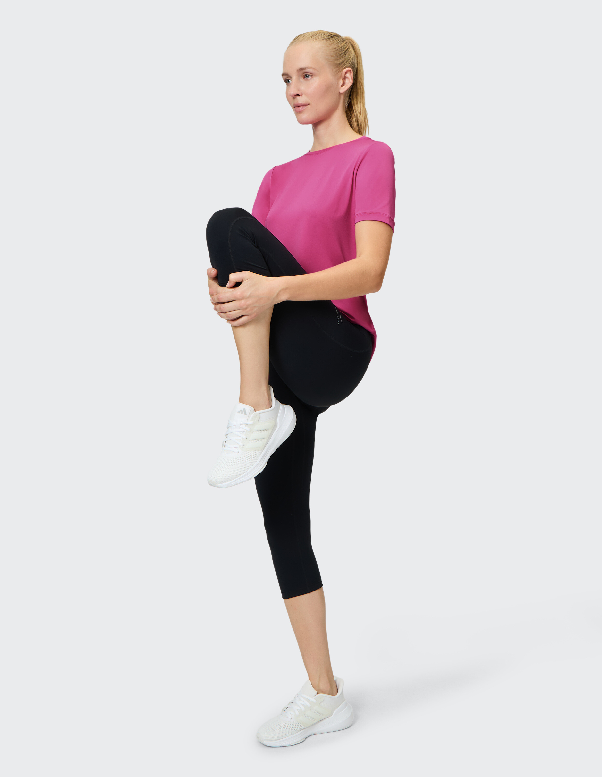 Frau in rosa T-Shirt und schwarzen Leggings beim Stretching in bequemer Freizeitkleidung.