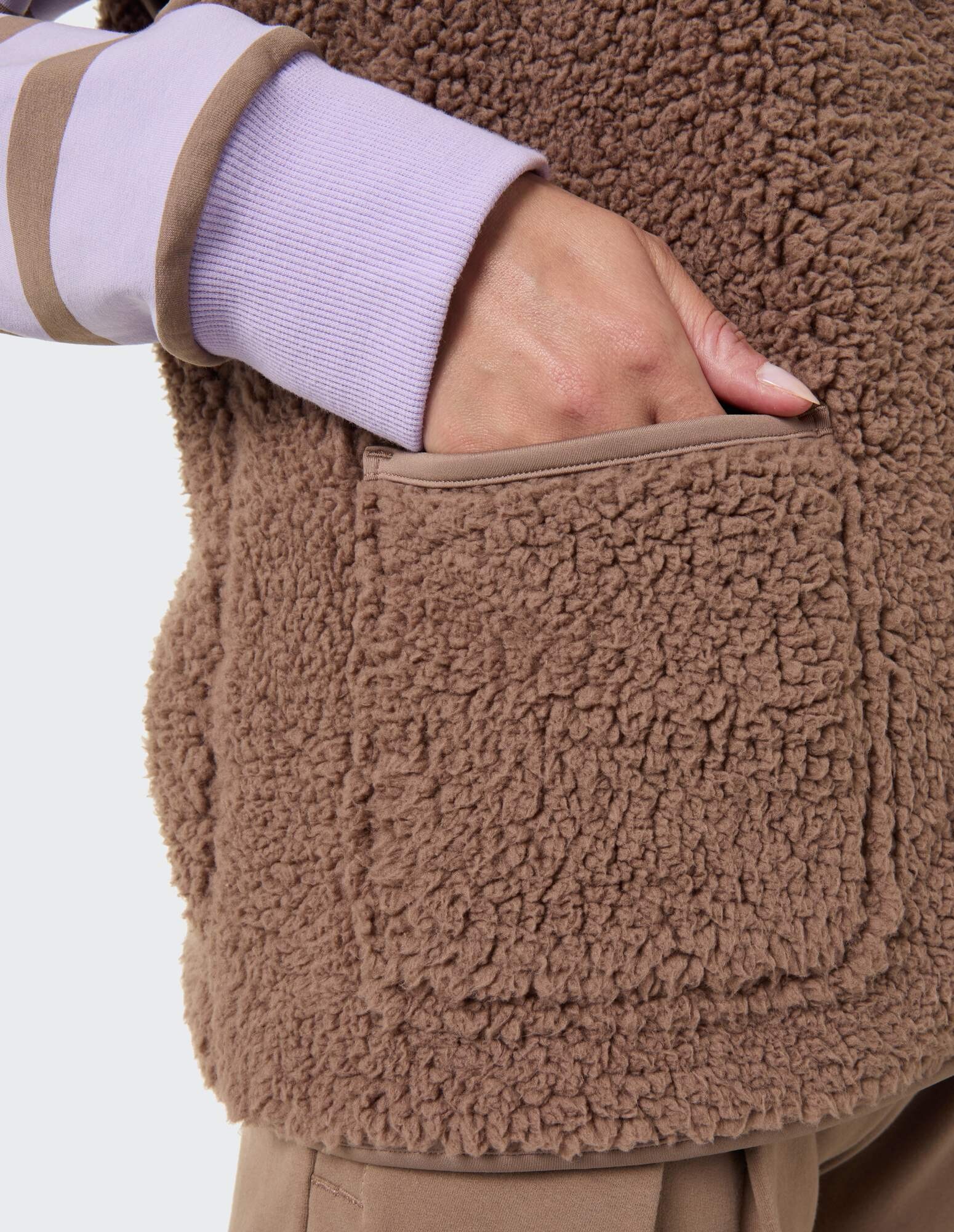 Nahaufnahme einer kuscheligen braunen Fleeceweste mit einer Hand in der Tasche.