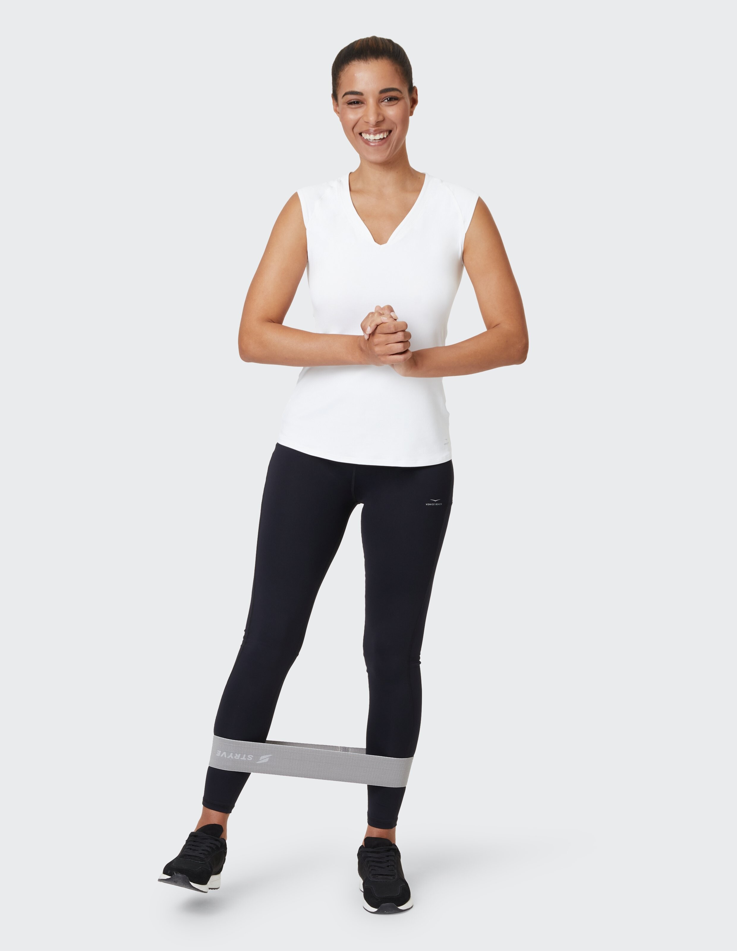 Frau in weißem Tanktop und schwarzen Leggings trainiert mit einem grauen Widerstandsband.