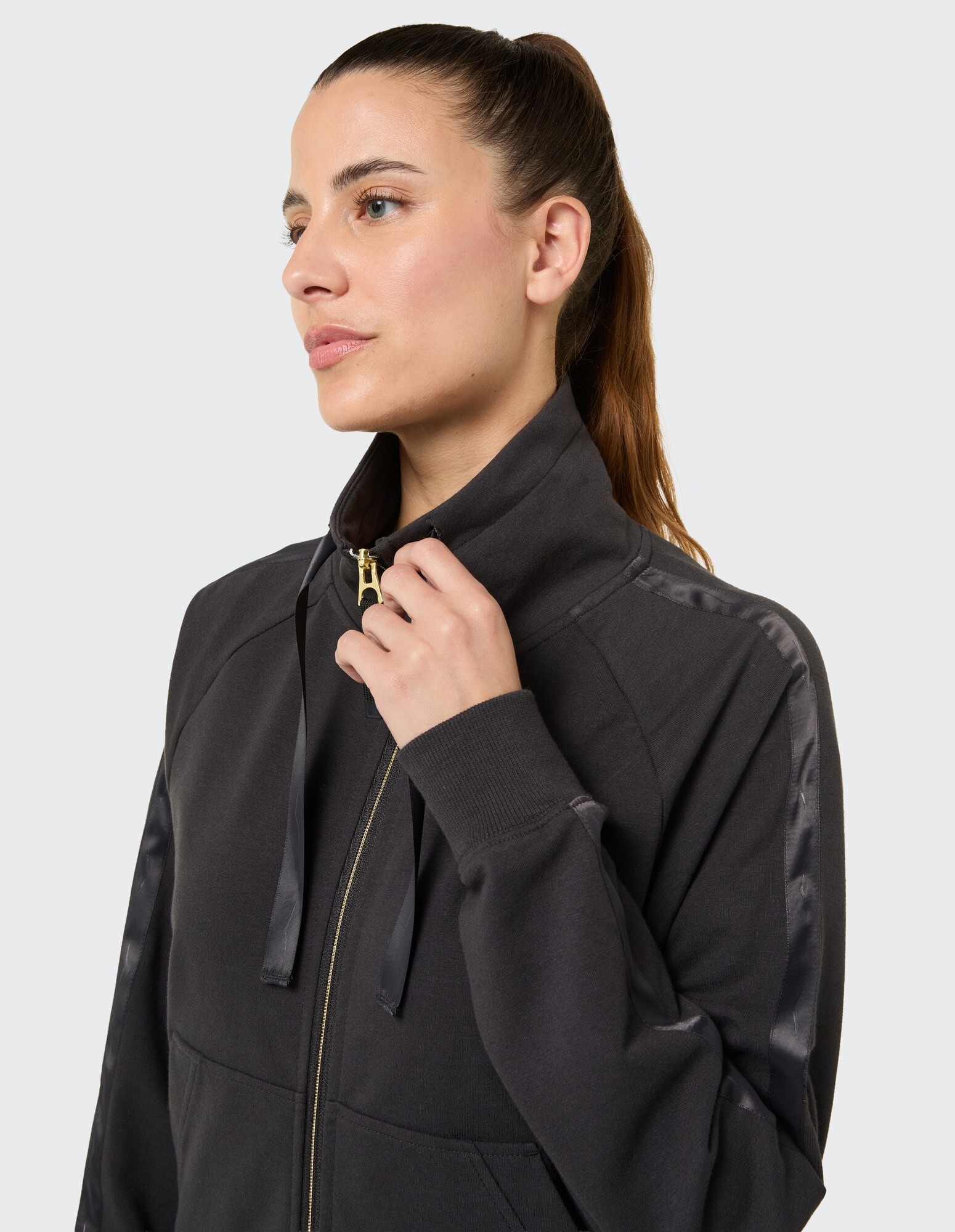 Nahaufnahme einer Frau in einem dunklen Kapuzenpullover mit Reißverschluss und Satindetails.