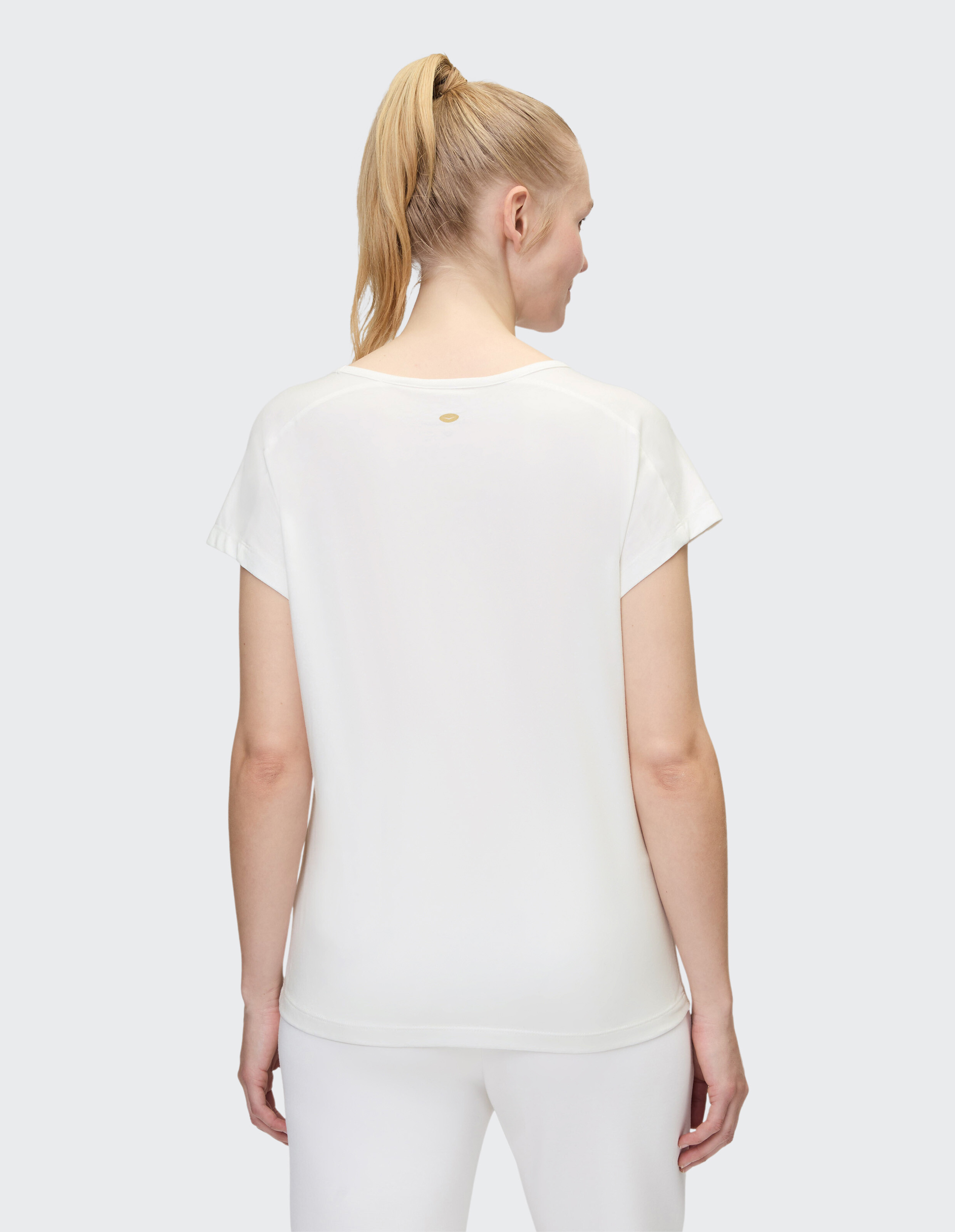 Frau trägt ein weißes, lässiges T-Shirt mit kleinem Logo-Detail, Rückansicht.