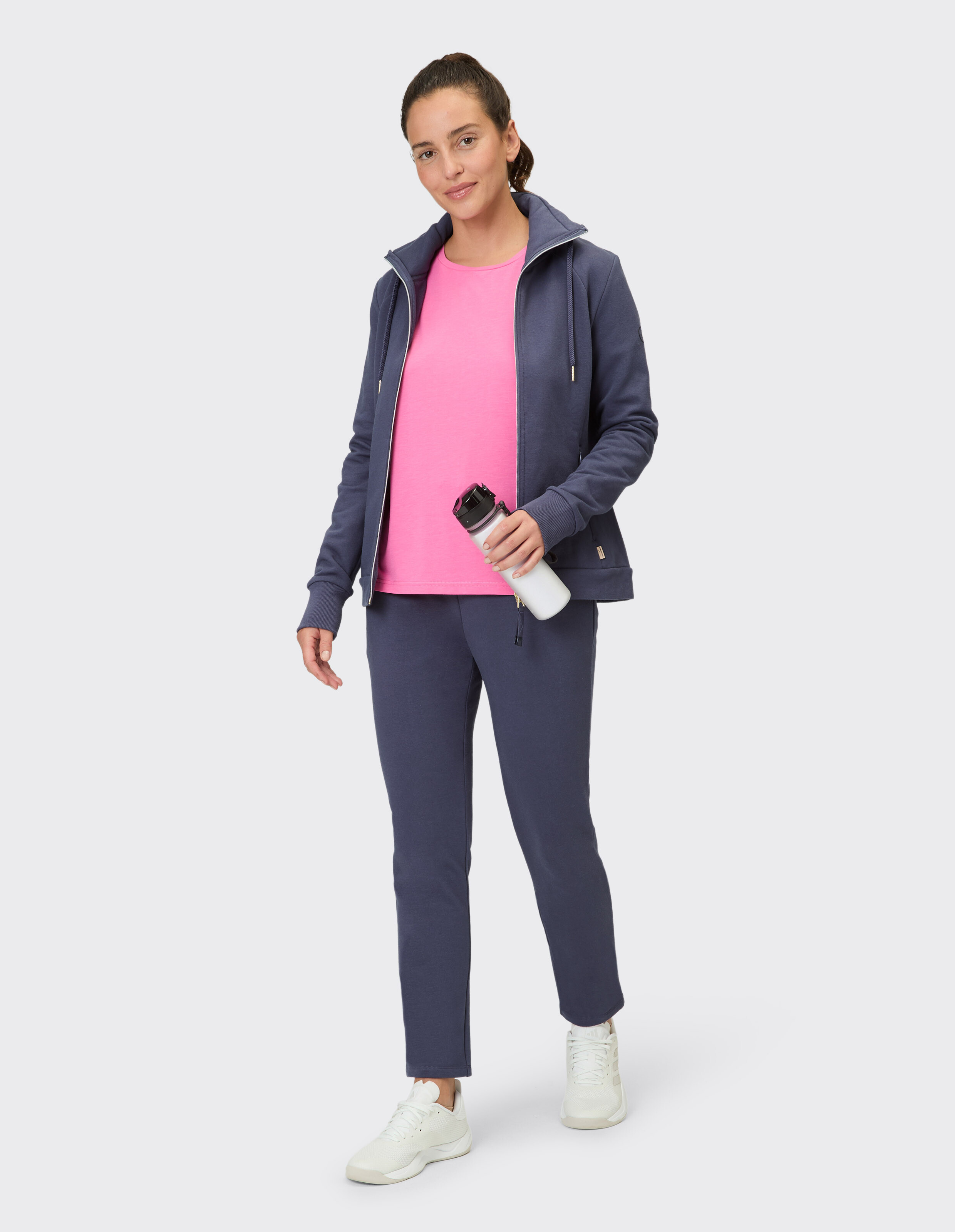 Frau im dunkelblauen Freizeitoutfit mit rosa Oberteil und einer Wasserflasche in der Hand.