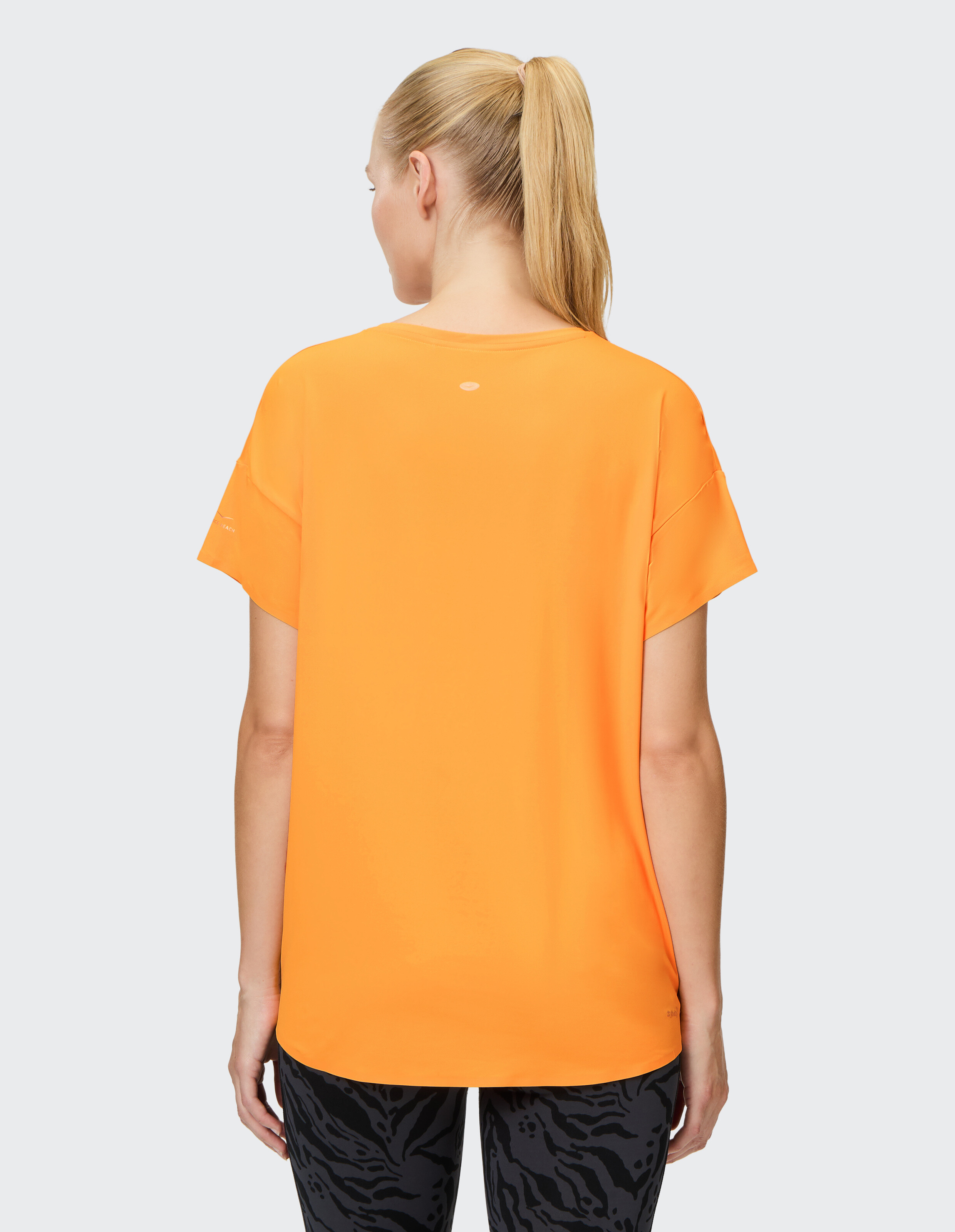 Rückansicht einer Frau in einem leuchtend orangefarbenen Freizeit-T-Shirt und gemusterten Leggings.