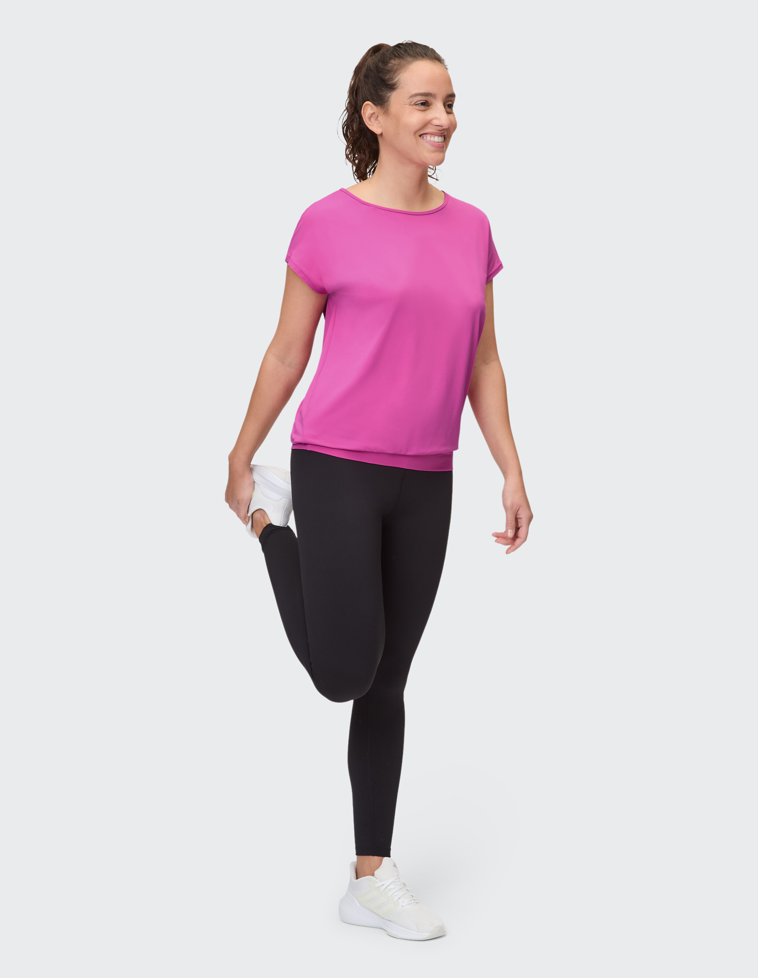 Frau in rosa Top und schwarzen Leggings dehnt sich in lässiger Atmosphäre.