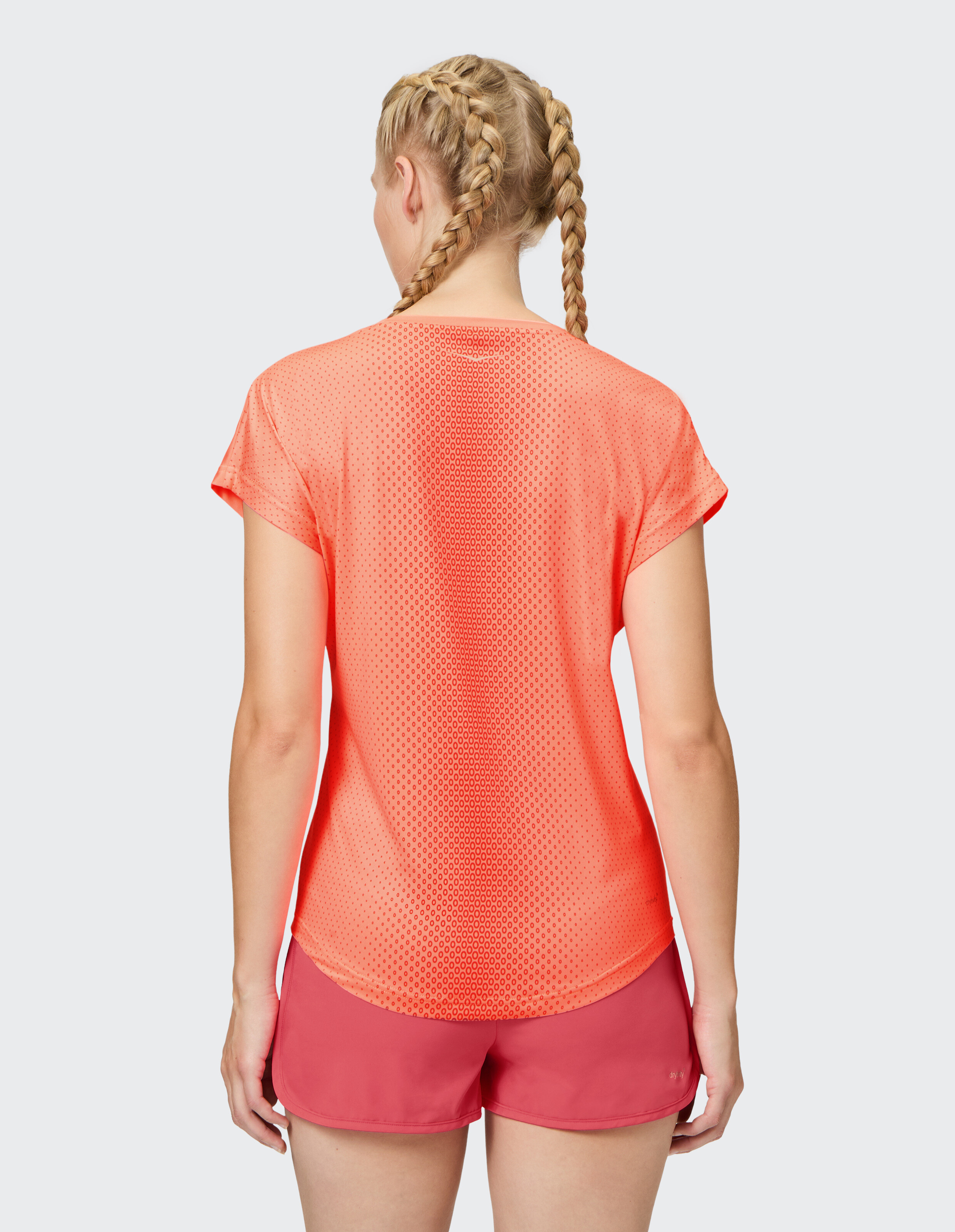 Frau trägt ein korallengemustertes Sport-T-Shirt und rote Shorts, Rückansicht.