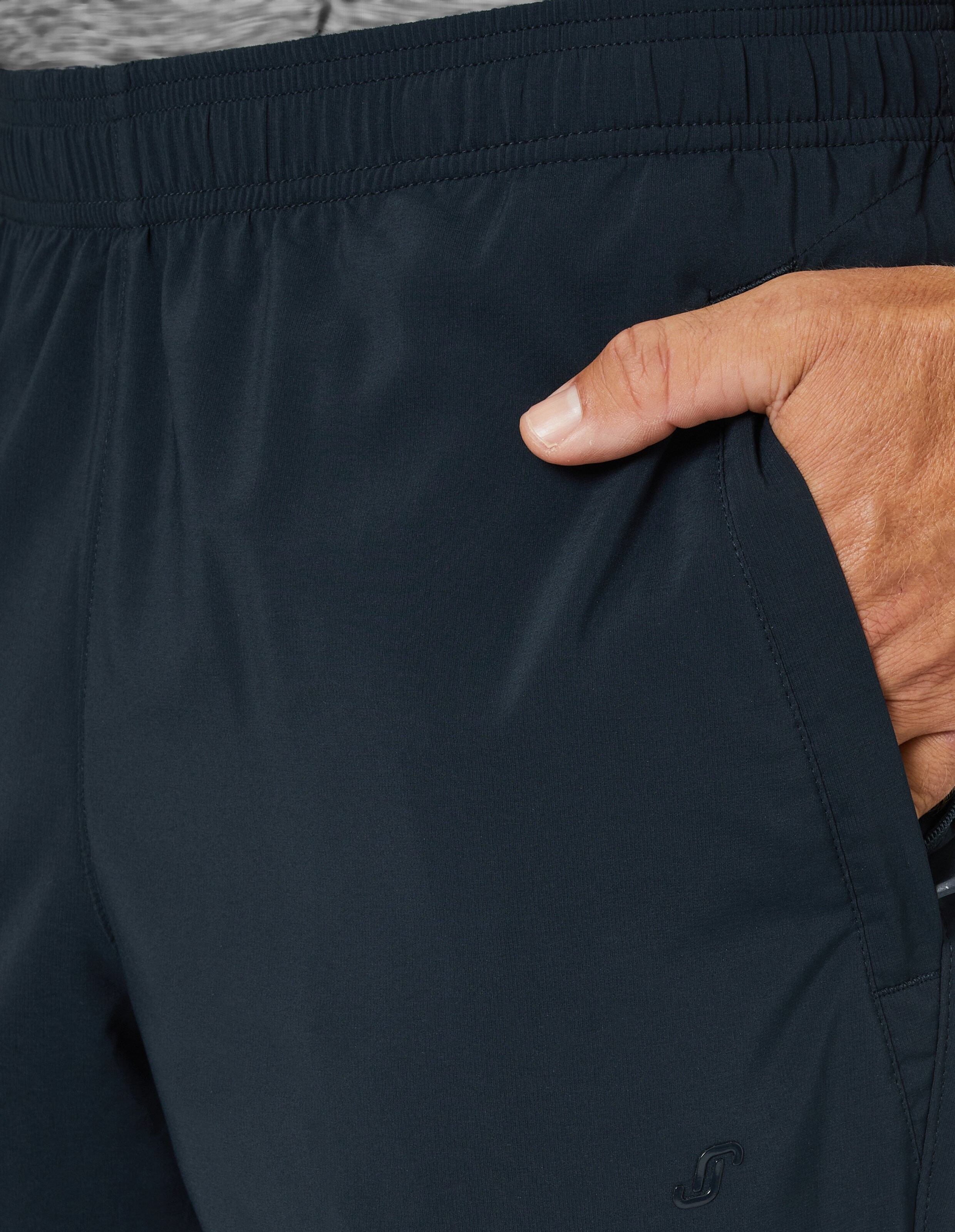 Nahaufnahme einer Hand, die in die Tasche einer dunkelblauen Jogginghose greift, mit elastischem Bund und subtilen Nähten.