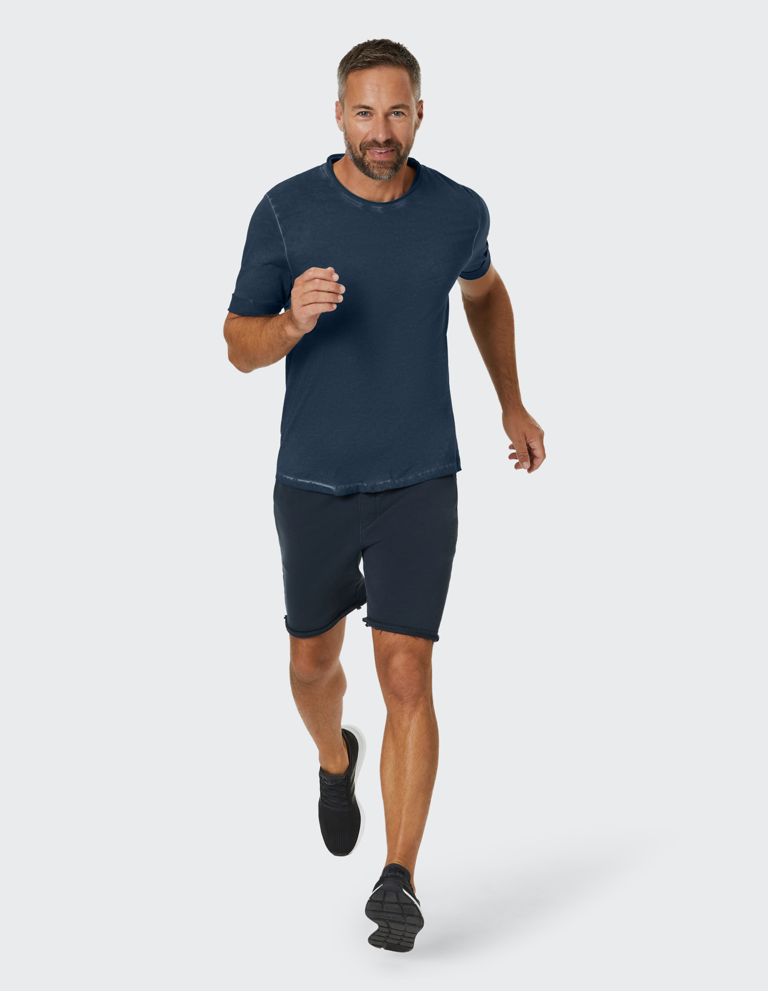 Mann in dunkelblauem Freizeit-T-Shirt und Shorts läuft in entspannter Atmosphäre.