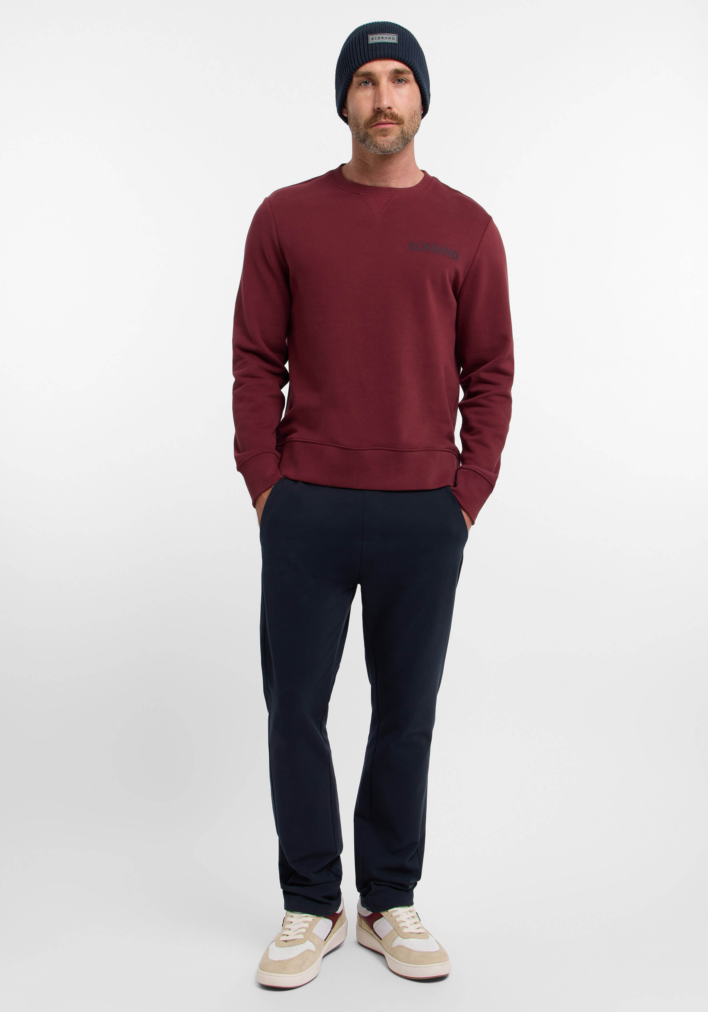 Mann in kastanienbraunem Sweatshirt und dunkelblauer Hose, lässig gestylt.