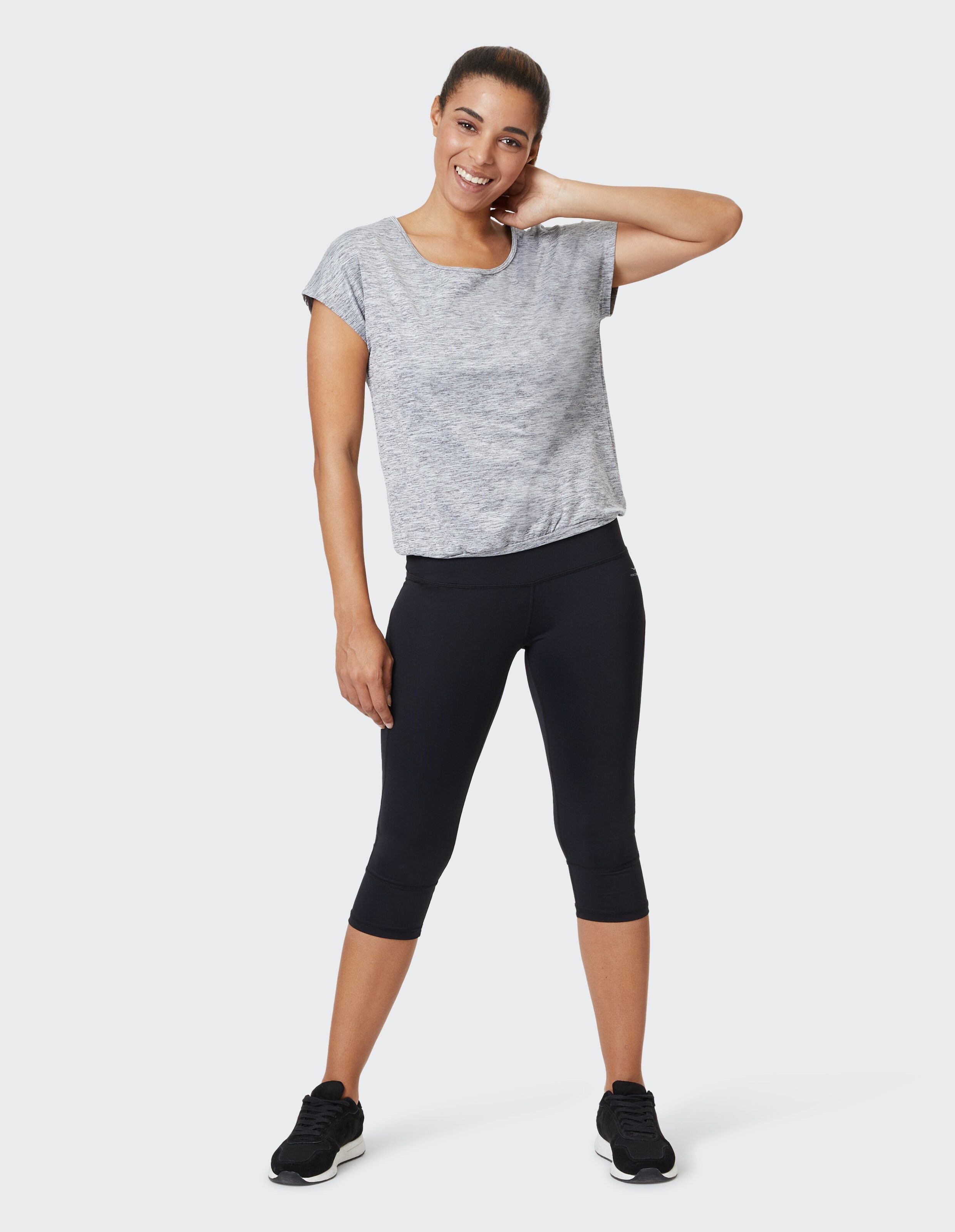 Frau in einem grauen Freizeitoberteil und schwarzen Capri-Leggings, lächelnd selbstbewusst.
