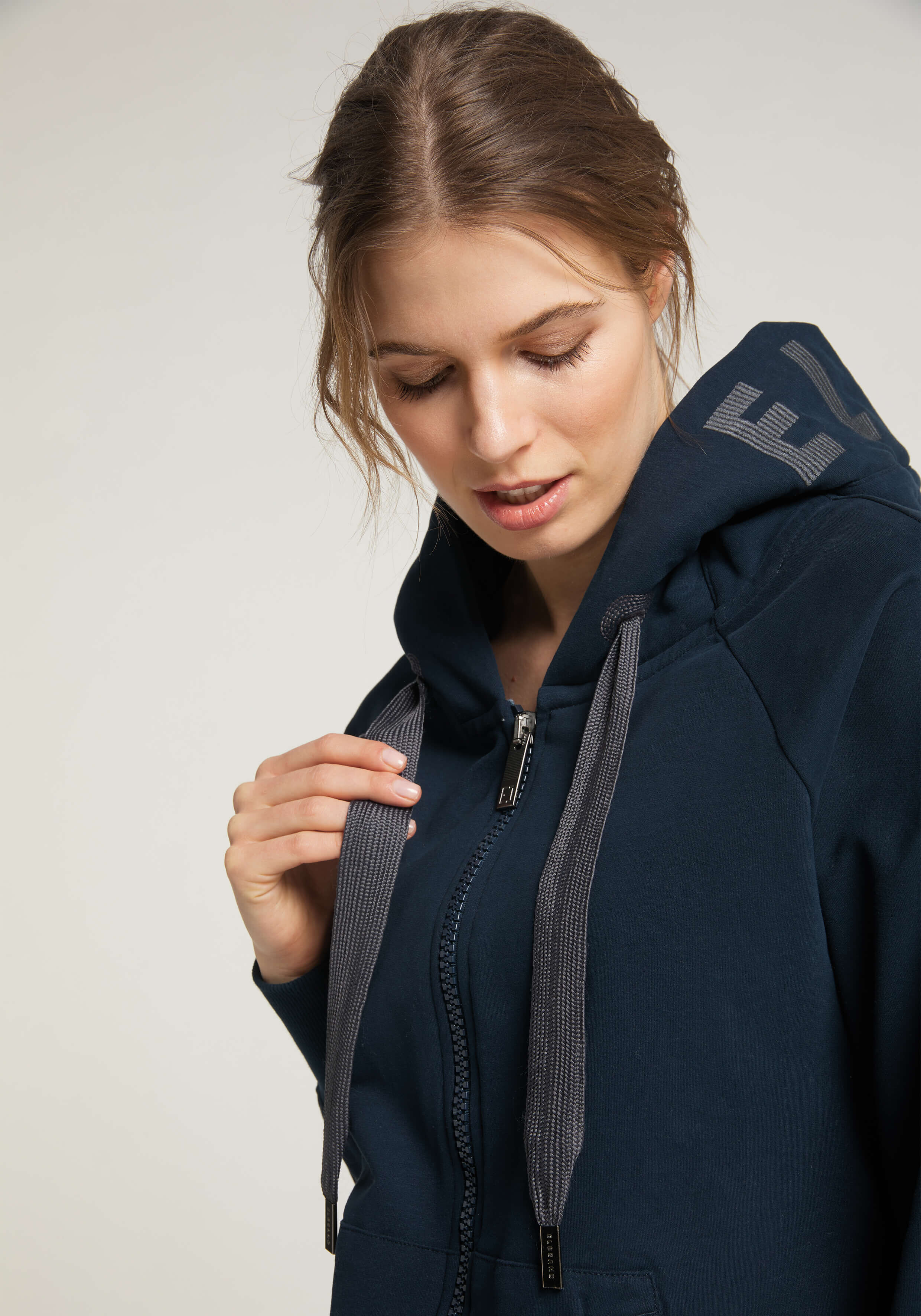 Frau in einem dunkelblauen Kapuzenpullover mit Reißverschluss und grauen Kordeln, die einen lässigen Stil zeigt.