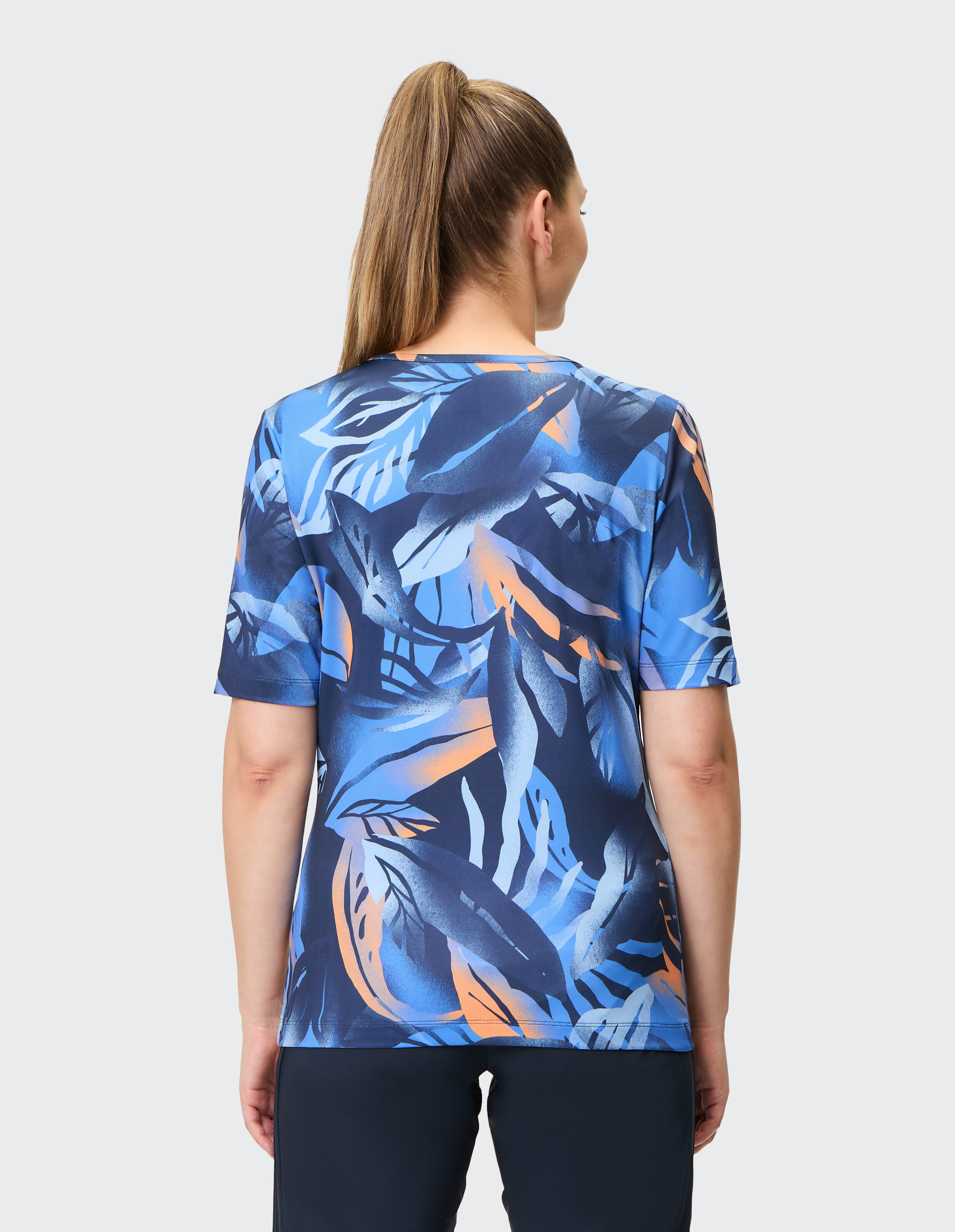 Blaues T-Shirt mit abstraktem, tropischem Blätterdesign in Blau und Orange auf dunkelblauem Hintergrund, kurzärmelig und rundhalsig.