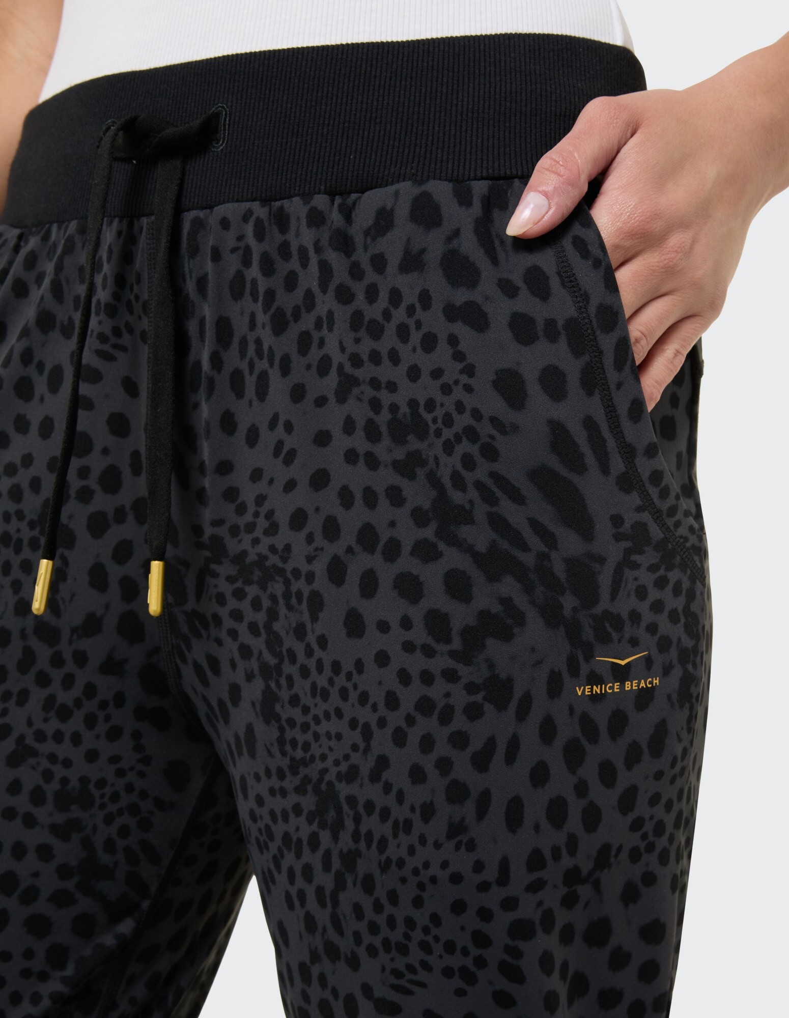 Nahaufnahme einer schwarzen Jogginghose mit Leopardenmuster, elastischem Bund und Logo.