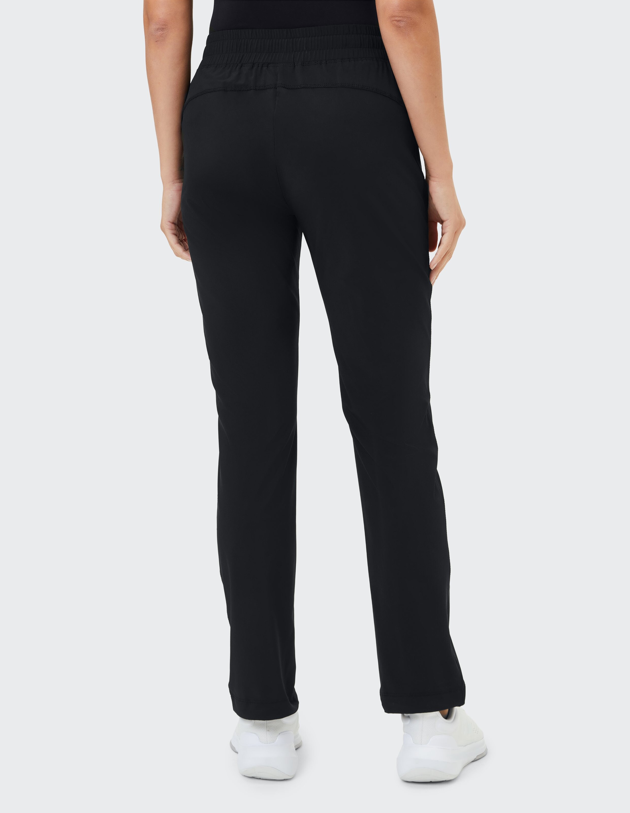 Rückansicht einer schwarzen Freizeithose mit elastischem Bund und weißen Turnschuhen.