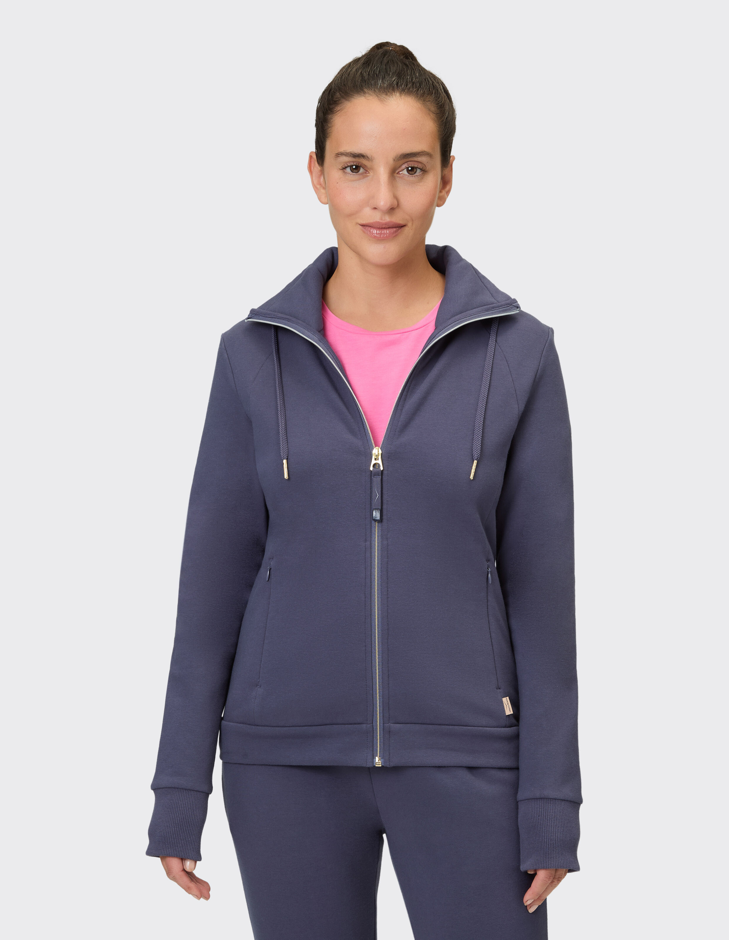 Frau in einem dunkelblauen Kapuzenpullover mit Reißverschluss und einem rosa Hemd darunter, stilvoll und bequem.