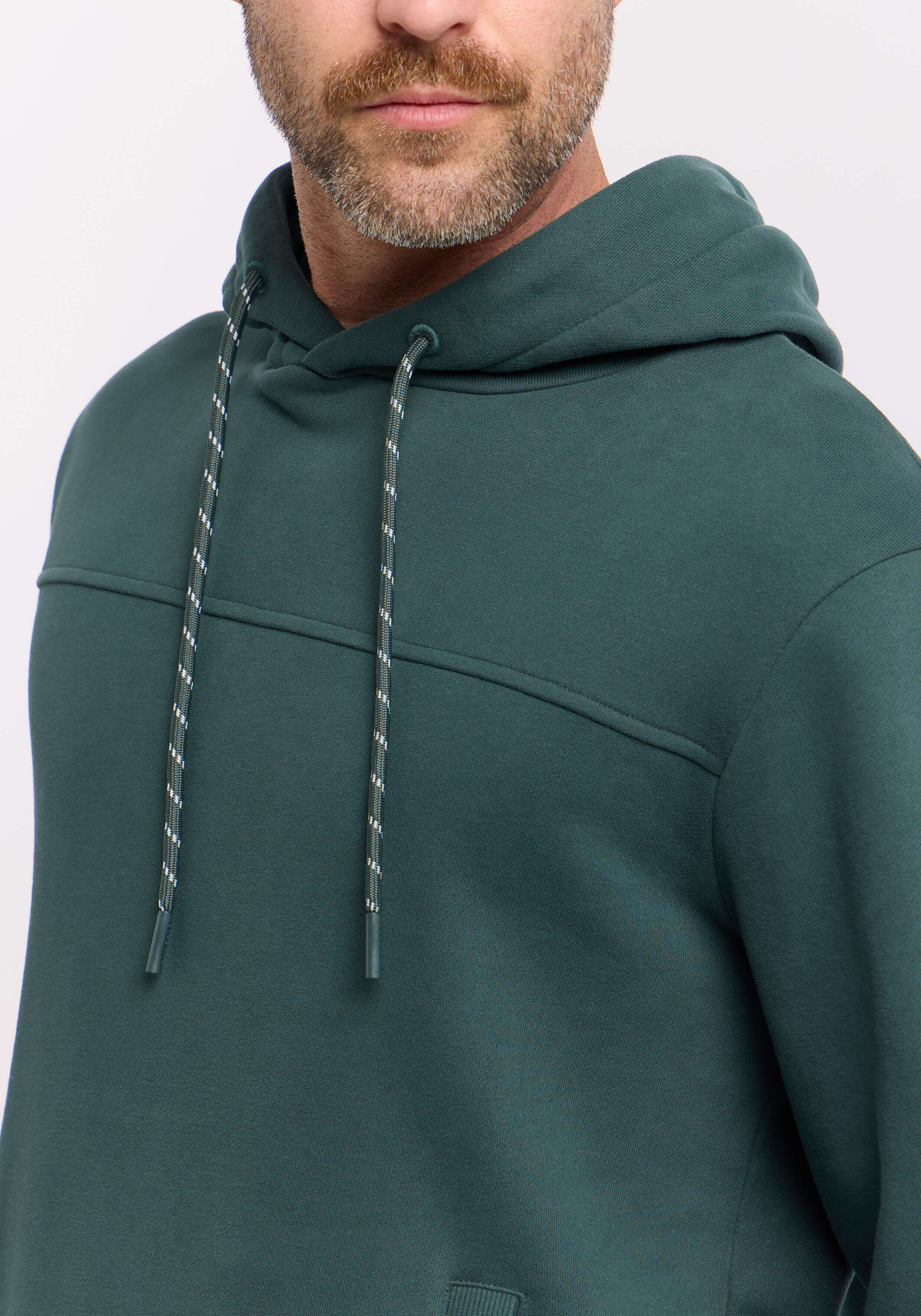 Mann trägt einen gemütlichen dunkelgrünen, lässigen Kapuzenpullover mit Kordelzug.